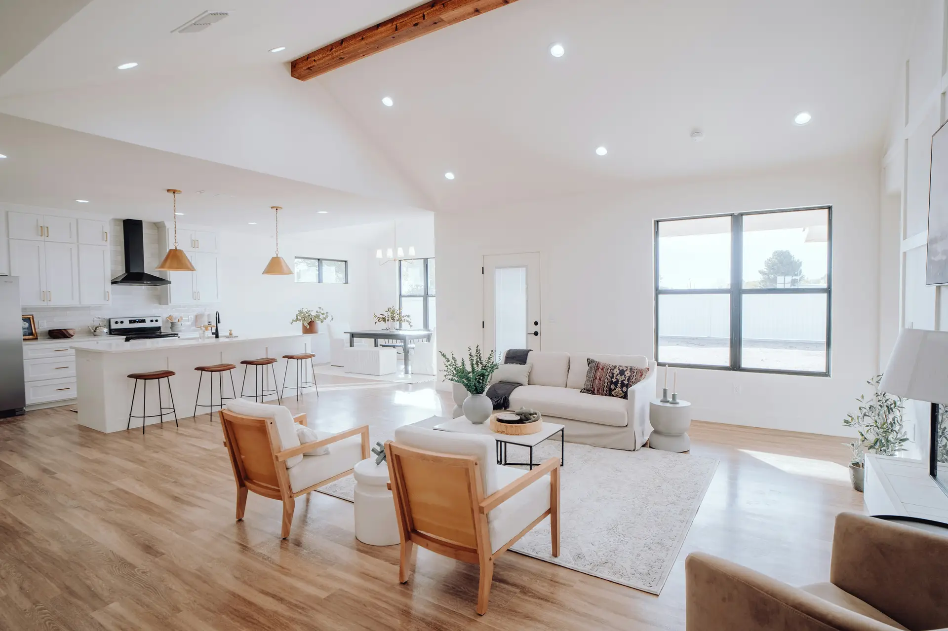 Bright open-concept home with a white kitchen featuring brass pendant lights and a long island, seamlessly flowing into a cozy living area with neutral furniture and large windows; the space offers kitchen ideas that prioritize open sightlines to living area for an airy, connected feel.