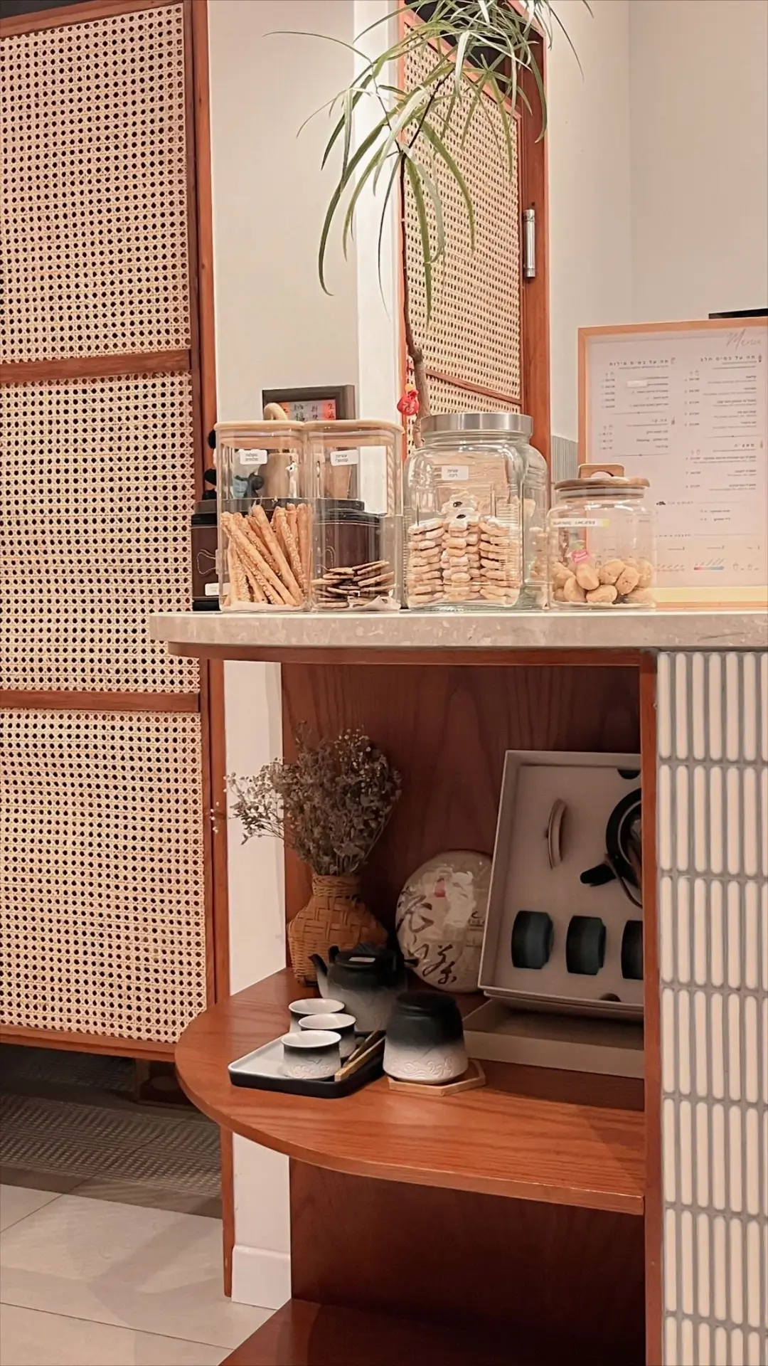 Warm, cozy corner with jars of snacks arranged neatly on a small counter, woven cabinet fronts, and shelves holding teaware and decor; the thoughtful layout showcases smart storage solutions and offers kitchen ideas for maximizing style and function in compact spaces.