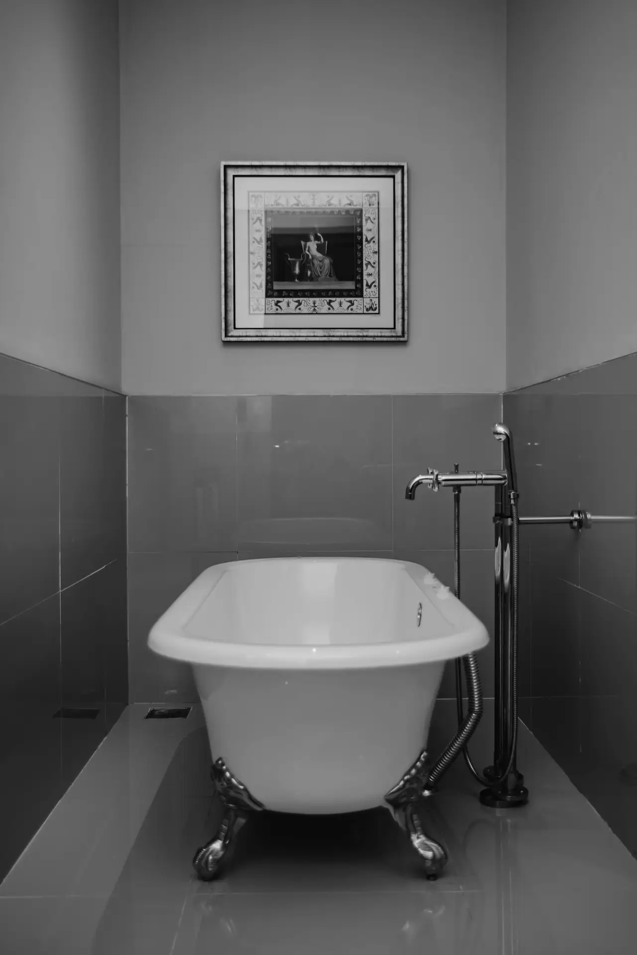 A monochrome bathroom scene featuring a classic clawfoot tub centered against tiled walls, paired with a floor-mounted faucet and framed artwork above, showcasing elegant bathroom ideas with a tub that balance traditional charm with a clean, minimalist layout.