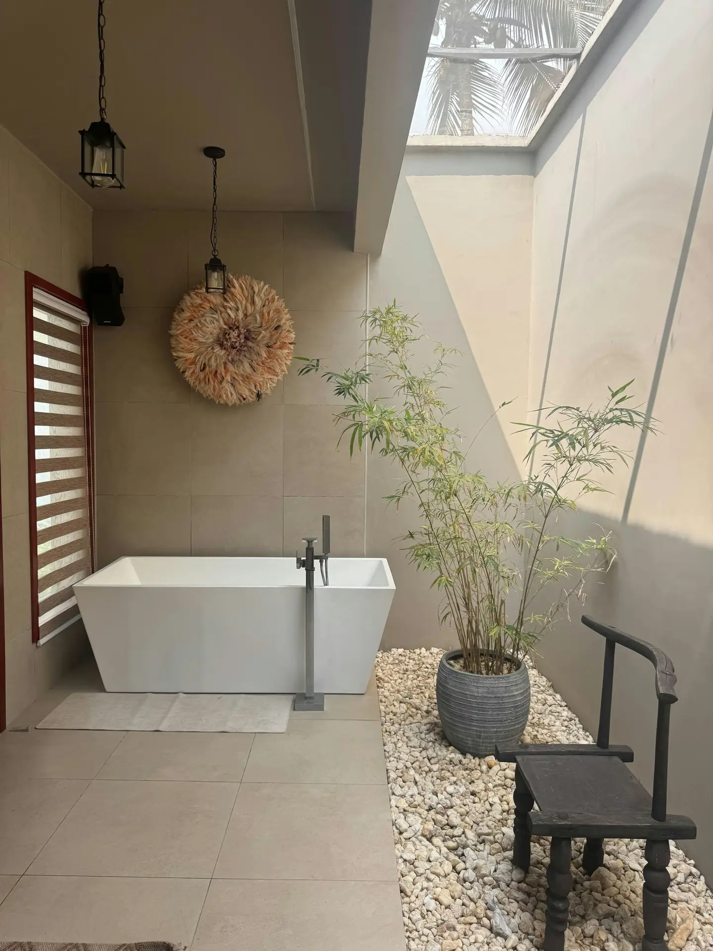 A serene, spa-like bathroom features a free standing rectangular tub placed beneath a skylight, surrounded by neutral tiles, soft hanging lights, and a potted bamboo plant on decorative gravel, offering relaxed bathroom ideas with a tub that blend clean lines, natural textures, and indoor-outdoor harmony.