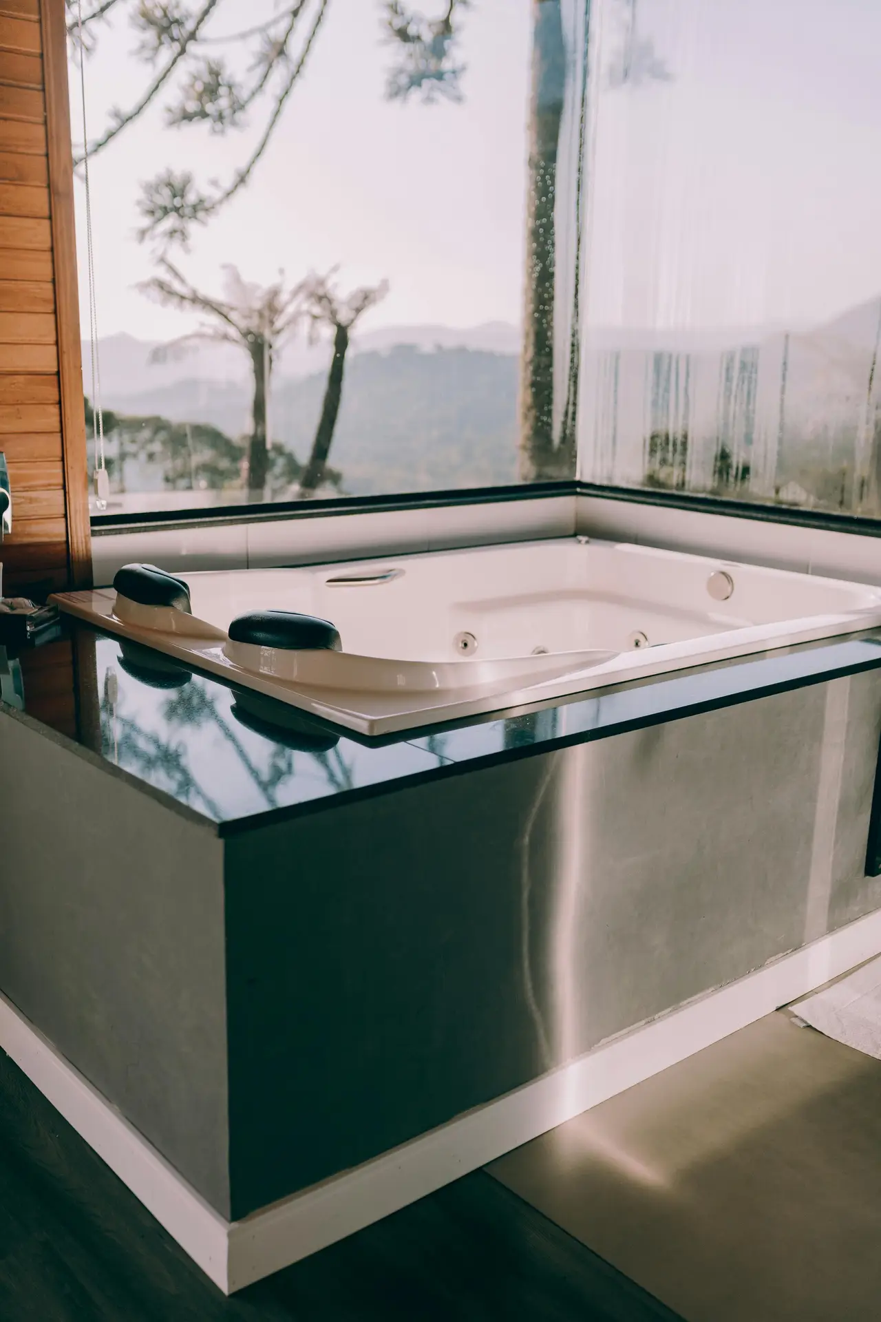 A modern spa-style bathroom features an embedded rectangular tub set into a sleek platform, positioned beside large corner windows that open up to a peaceful forest view, showcasing calm bathroom ideas with a tub that focus on clean lines, natural light, and a seamless built-in design.