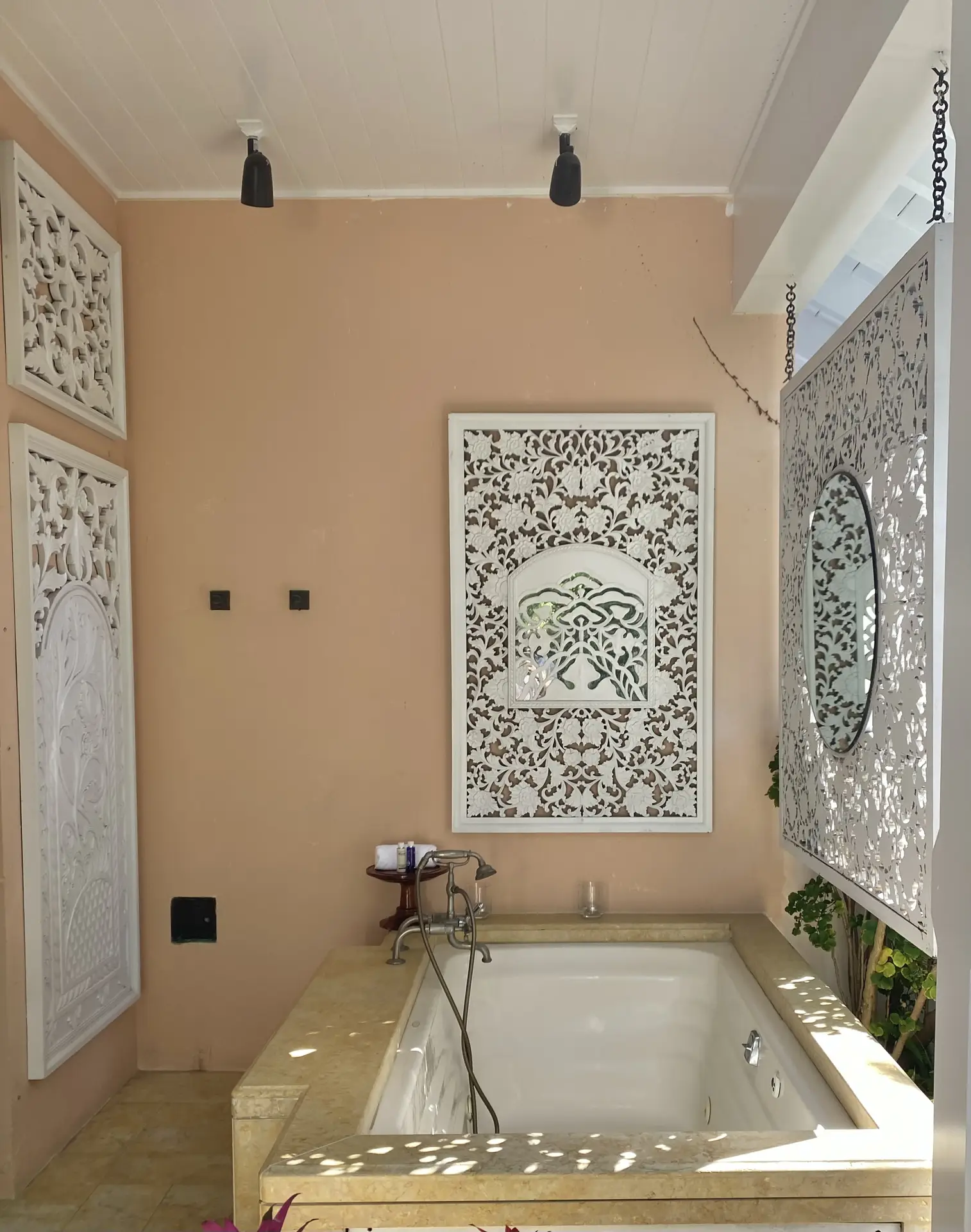 A serene bathroom setting showing a tub embedded in stone with a smooth, light-colored surround, decorative carved wall panels, warm neutral walls, and soft natural light filtering through, offering timeless bathroom ideas with a tub that blend architectural detail with a calm, spa-like atmosphere.