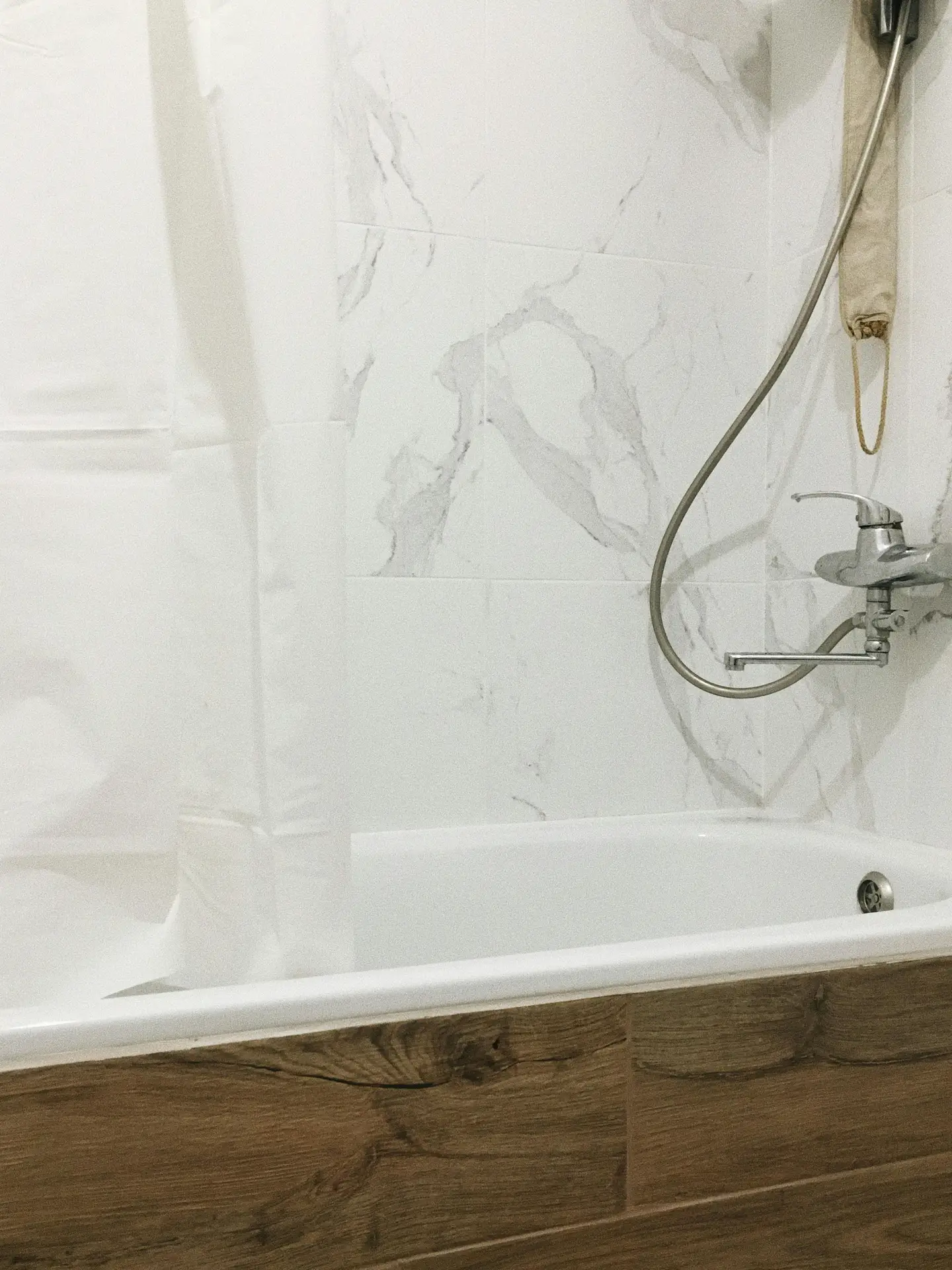 A modern bathtub with clean white edges is paired with warm wooden paneling on the front and marble-look wall tiles behind, showcasing bathroom ideas with a tub that blend natural textures and a tub with wooden paneling for a balanced, timeless look.