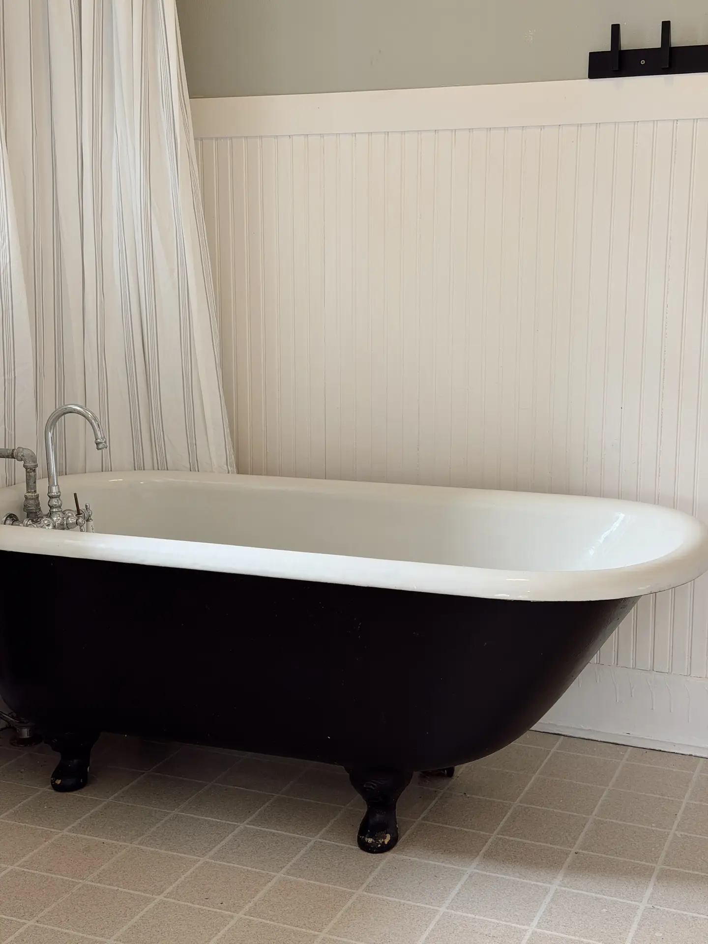 A classic black-and-white vintage tub with curved edges and claw-style feet stands against a light paneled wall, paired with traditional metal fixtures and soft neutral flooring, illustrating timeless bathroom ideas with a tub that blend nostalgic charm with clean, versatile design.