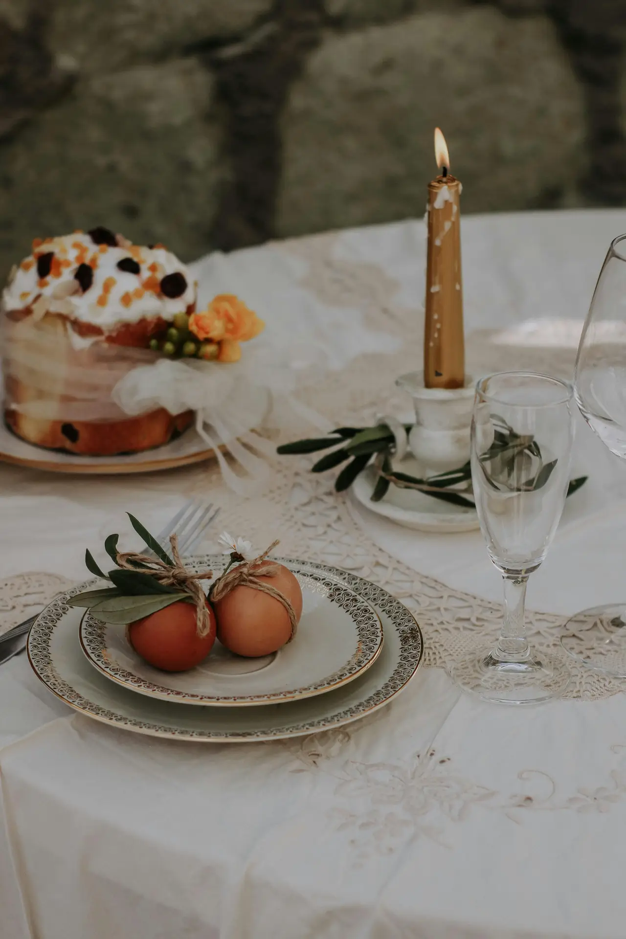 Soft and elegant easter table decor showcasing simple egg decor with greenery placed on patterned plates, complemented by a delicate lace tablecloth, clear glassware, a lit taper candle, and a small festive cake creating a cozy spring table setting.