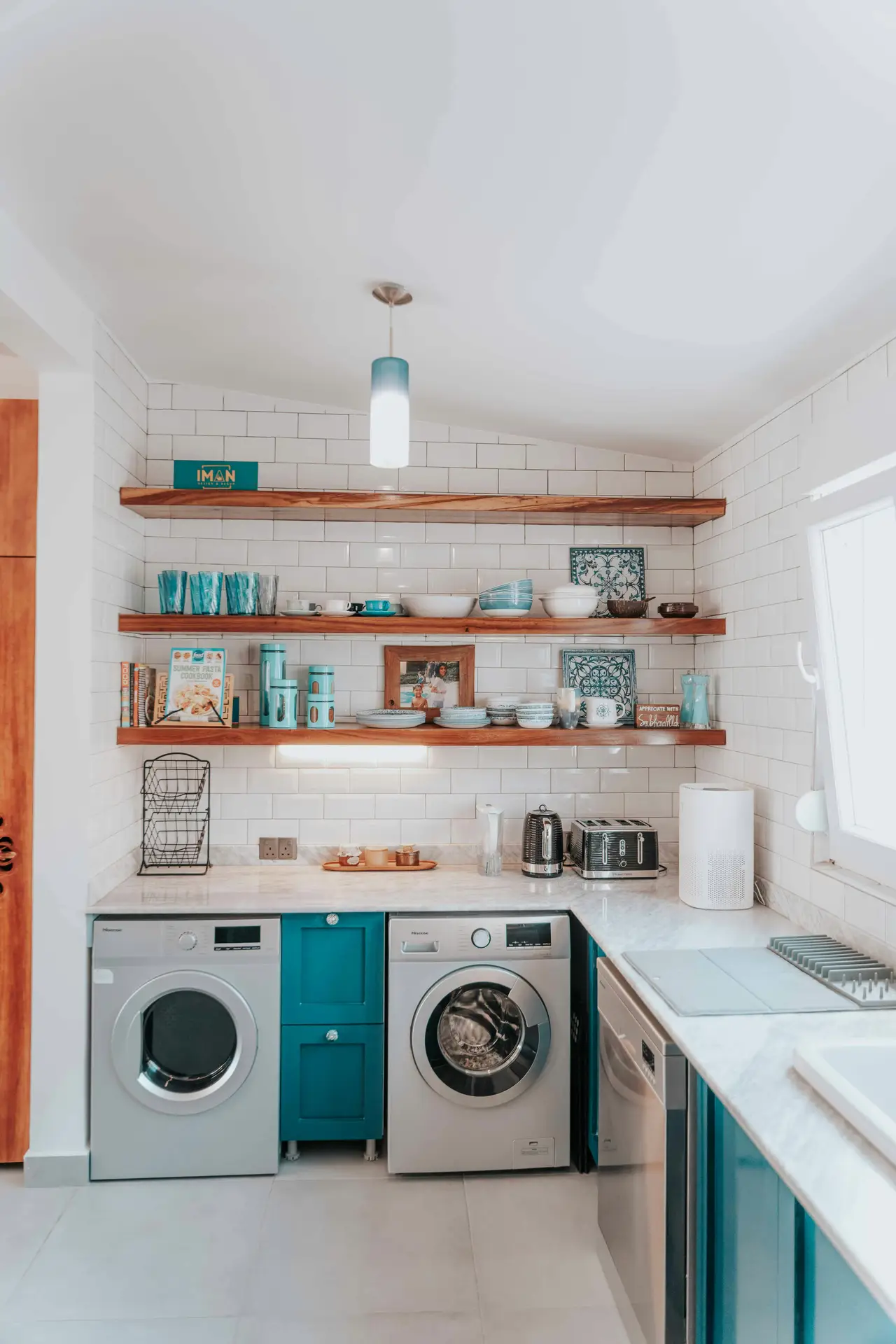 A bright kitchen space where a washer and dryer are seamlessly built into lower cabinets beneath a marble-look countertop, complemented by open wooden shelves with dishes and decor, illustrating laundry room organization ideas that show how laundry integrated in kitchen layouts can feel cohesive and practical.