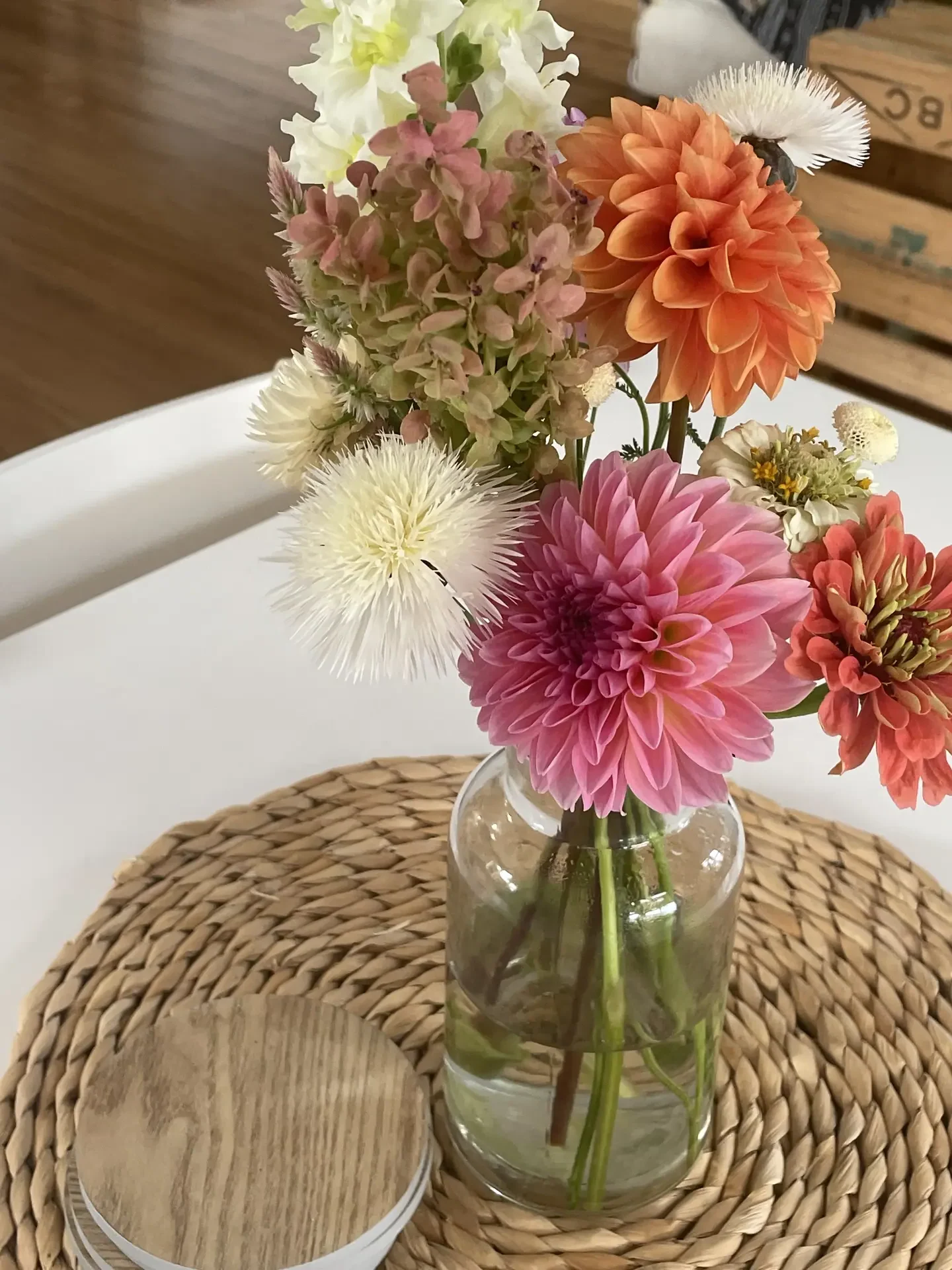 Living room coffee table decor ideas for spring featuring simple fresh flowers arranged in a clear glass vase, showcasing a colorful mix of pink, peach, and white blooms placed on a woven rattan tray with a wooden coaster, creating a relaxed, natural look that works with both modern and cozy living room styles.