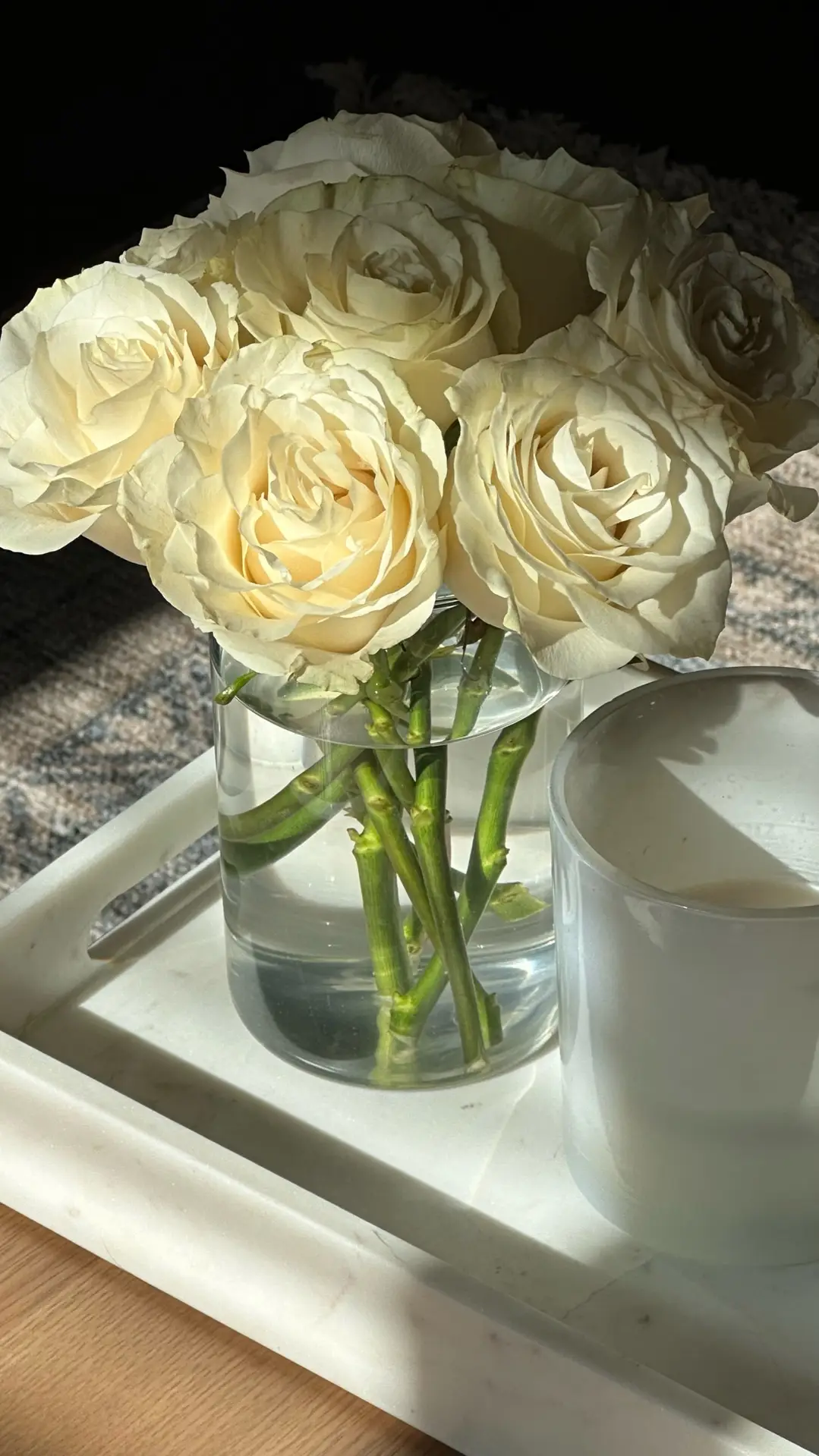 Simple living room coffee table decor ideas for spring featuring white flowers arranged in a clear glass vase on a light tray, paired with a minimal candle and soft natural light for a fresh, timeless look that works in many interior styles.