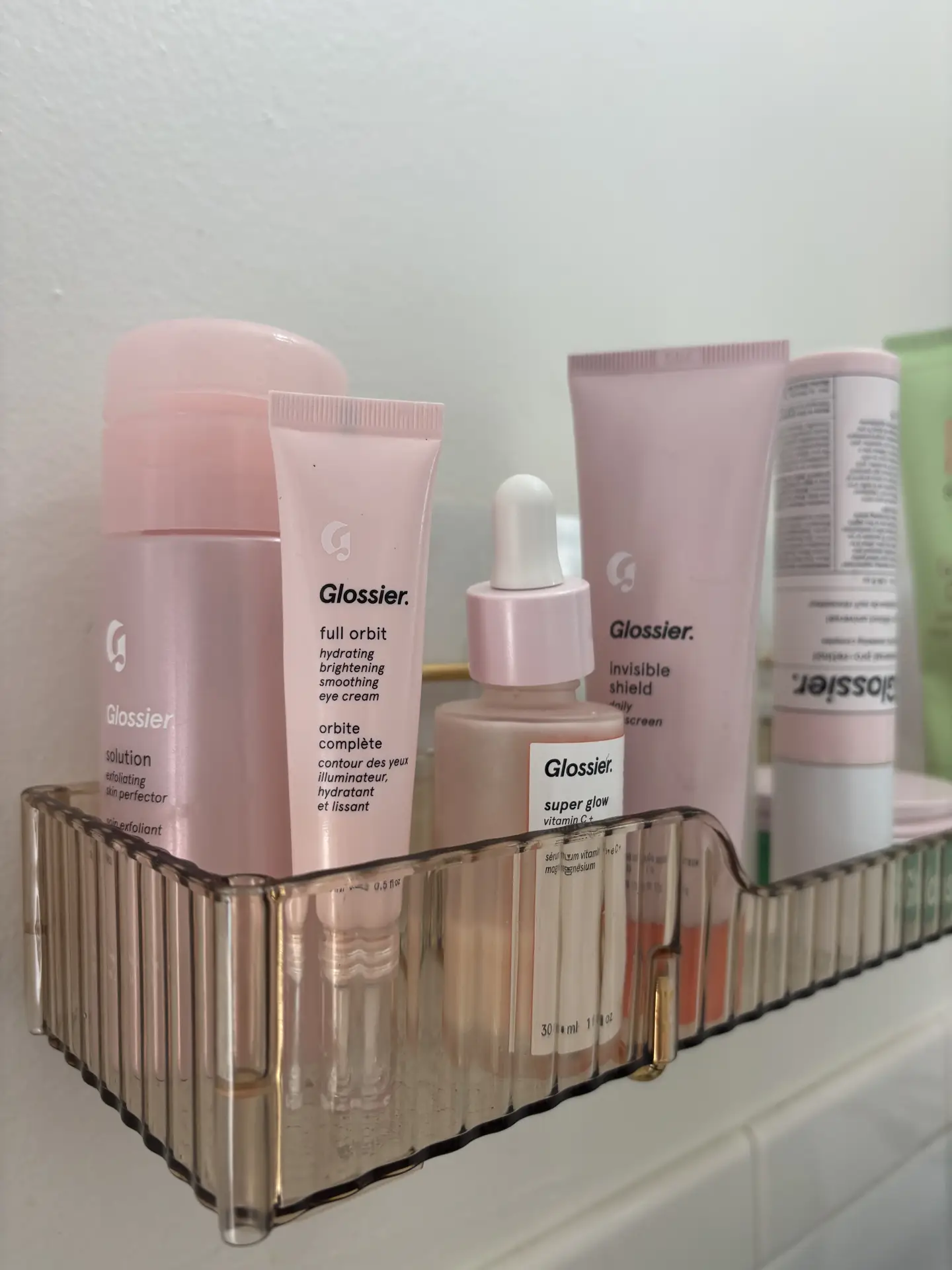 A clear acrylic bin neatly holds several pink-toned skincare bottles and tubes inside a bathroom cabinet, showing organization ideas for small spaces by using acrylic bins inside cabinets to keep everyday beauty products visible, sorted, and easy to reach.