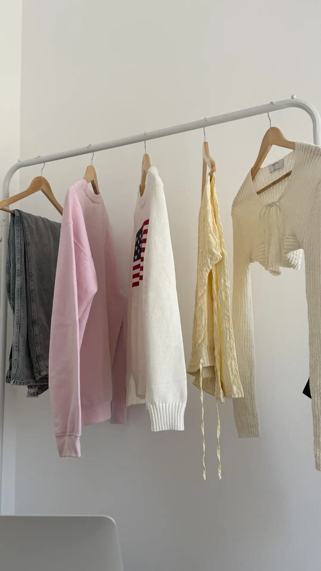 A simple clothes rack set against a neutral wall holds a small selection of neatly spaced garments on wooden hangers, showing organization ideas for small spaces by using an open clothes rack to store everyday outfits without the need for bulky wardrobes.