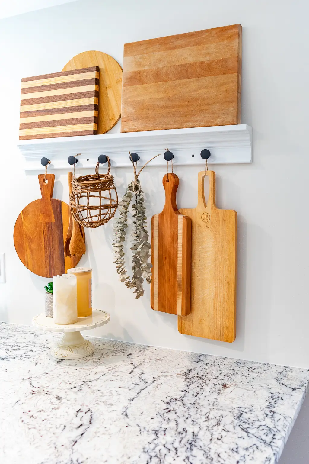 Bright kitchen corner showcasing organization ideas for small spaces, where you organize your cutting boards on hooks and shelves using a slim wall-mounted rail with wooden boards hanging neatly below and extra boards displayed above, adding both practical storage and warm decorative detail.