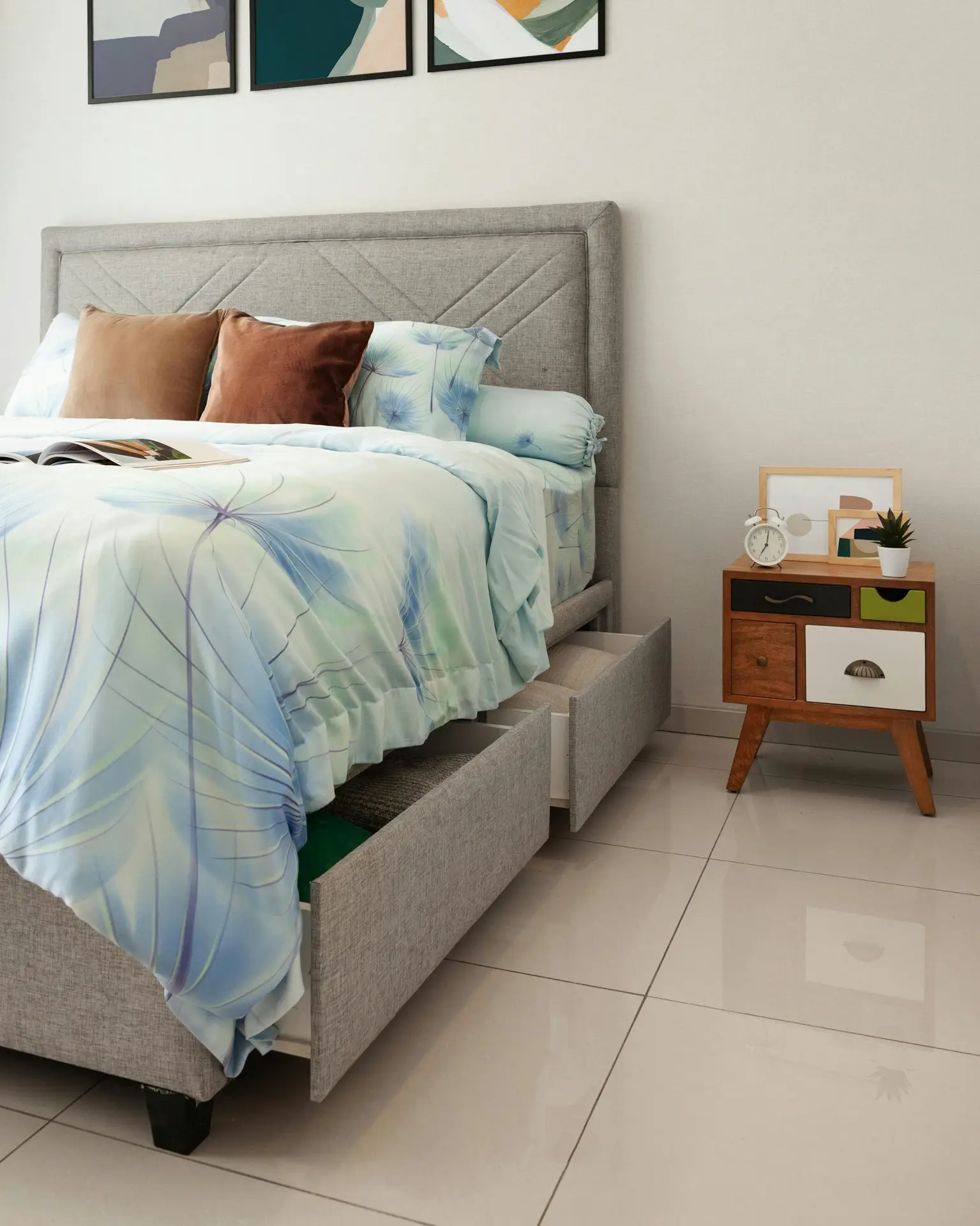 A modern bedroom with a soft upholstered bed featuring open pull-out bed drawers for hidden storage, paired with light bedding, accent pillows, and a compact bedside table, illustrating organization ideas for small spaces by keeping everyday items neatly tucked away without adding extra furniture.