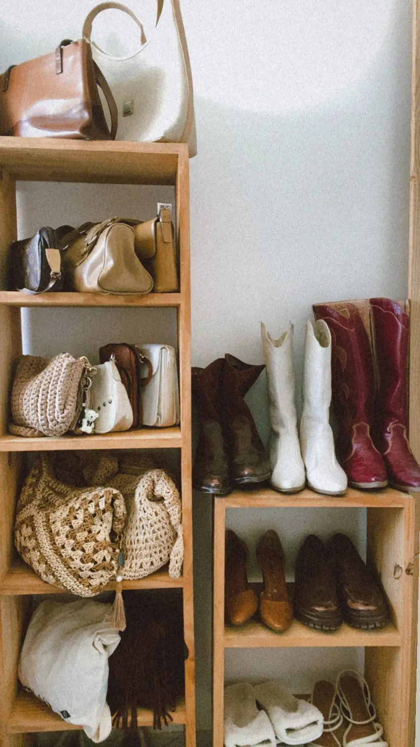 Vertical shoe cabinet styled with organization ideas for small spaces, featuring neatly arranged boots, flats, and handbags on open wooden shelves, with woven bags and folded accessories creating a functional yet decorative storage solution for a compact entryway or bedroom.