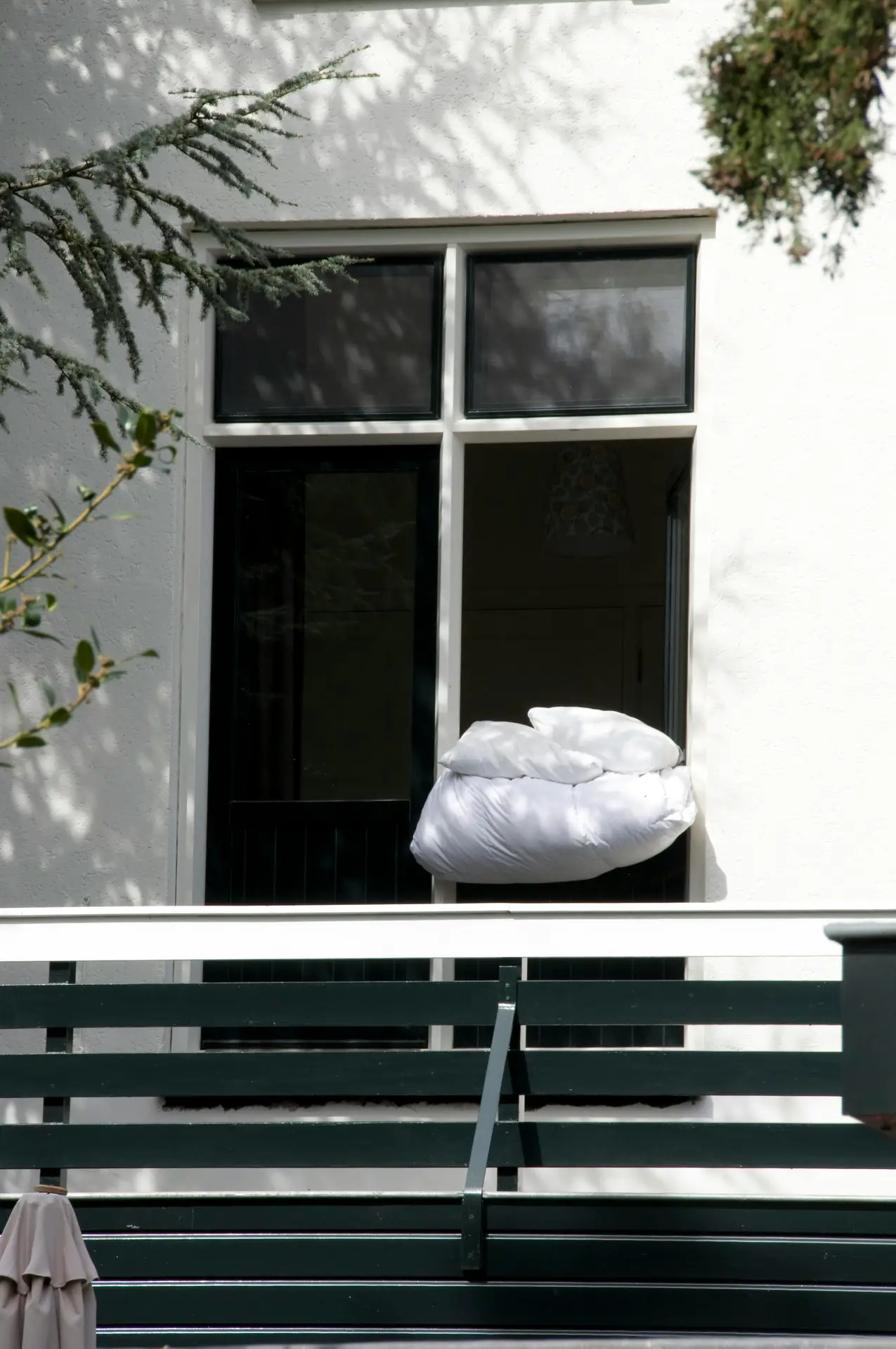 White bedding placed on a balcony railing in daylight outside a modern home, illustrating a spring cleaning checklist task to air out the bedding, freshen pillows and duvets, and let fabrics breathe in the open air.