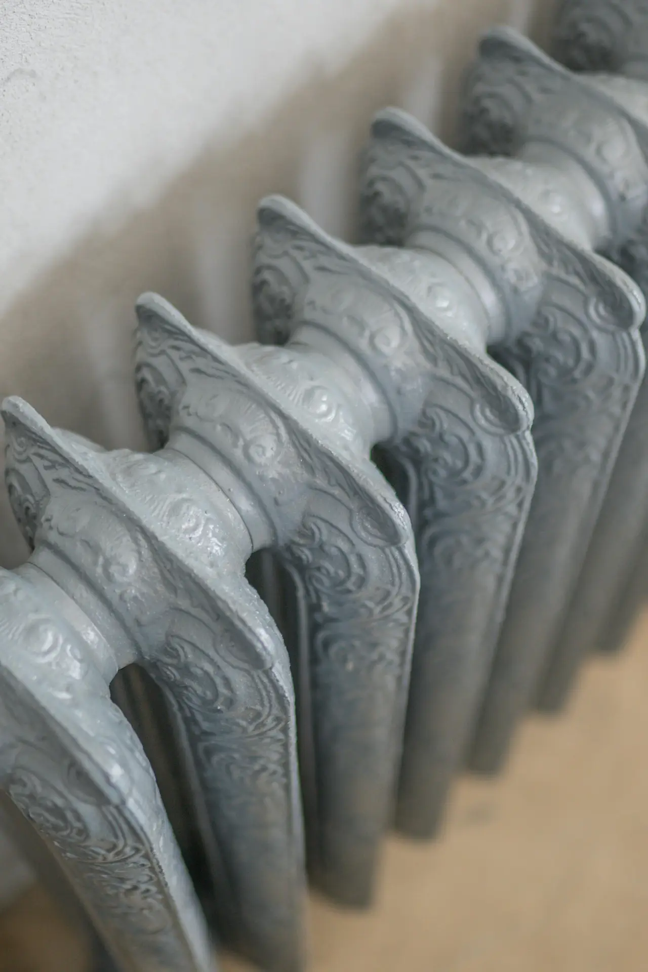 Close-up of a painted metal radiator with detailed fins along a light-colored wall, representing a spring cleaning checklist task focused on cleaning radiators, removing dust from heating elements, and refreshing hard-to-reach surfaces.