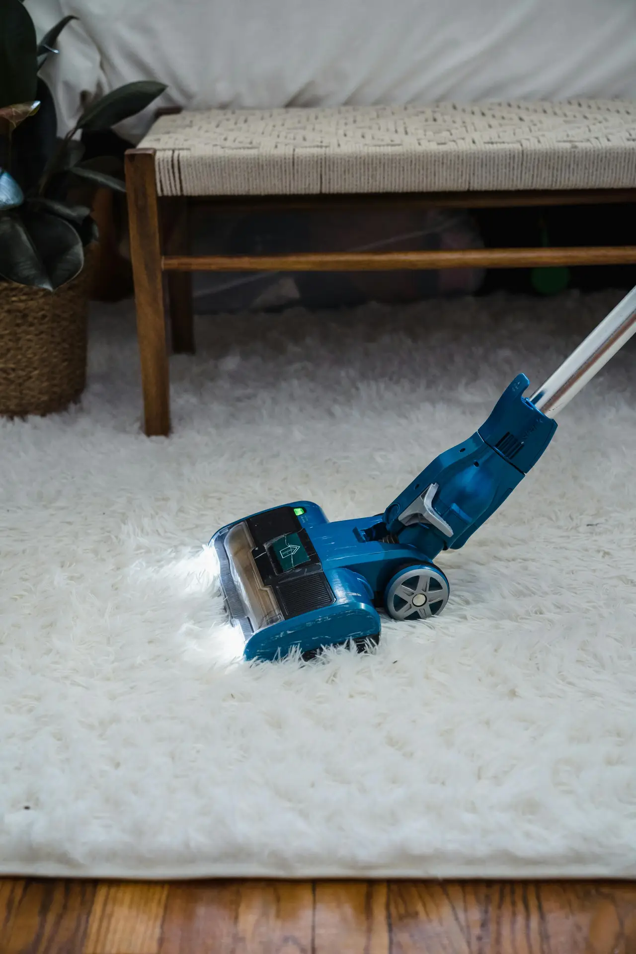 A compact carpet cleaning machine glides across a fluffy white rug in a cozy living space, highlighting a spring cleaning checklist step focused on deep cleaning of carpets to remove trapped dust and refresh soft flooring.