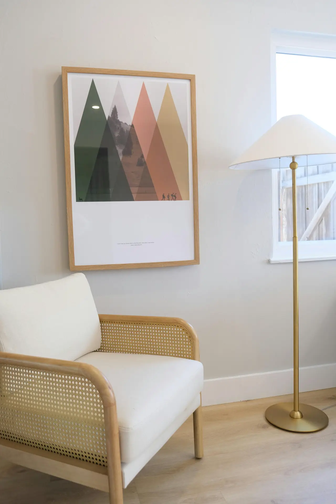 Bright spring decor ideas for living room showing a cozy seating corner with a white upholstered armchair featuring rattan accents, a light wood framed art print on the wall, and a slim floor lamp beside a window, creating an airy and relaxed atmosphere.