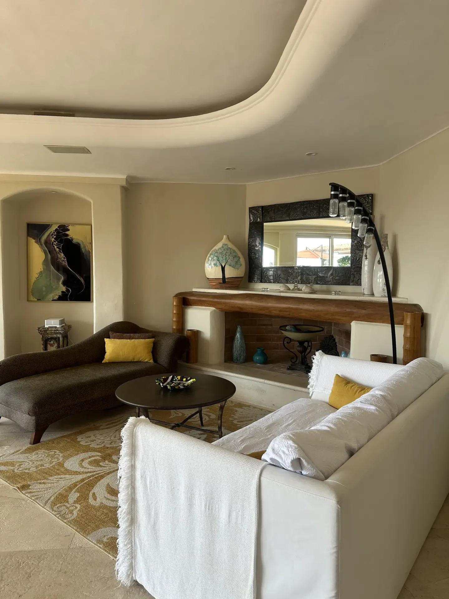 An inviting interior highlighting living room paint color ideas in a soft warm cream shade, featuring curved architectural details, a cozy seating arrangement with neutral sofas and accent pillows, a rustic wooden mantel with decor, layered lighting, and natural textures that create a relaxed, welcoming atmosphere.