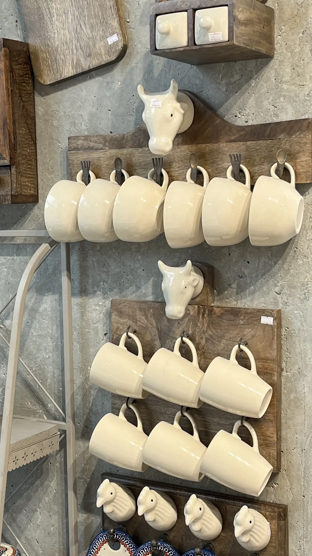 Whimsical wall display for modern farmhouse kitchens, featuring cute country details like white ceramic mugs hanging from rustic wooden boards, decorative animal-shaped hooks, and natural textures against a stone-look wall, creating a cozy and playful farmhouse-inspired accent.