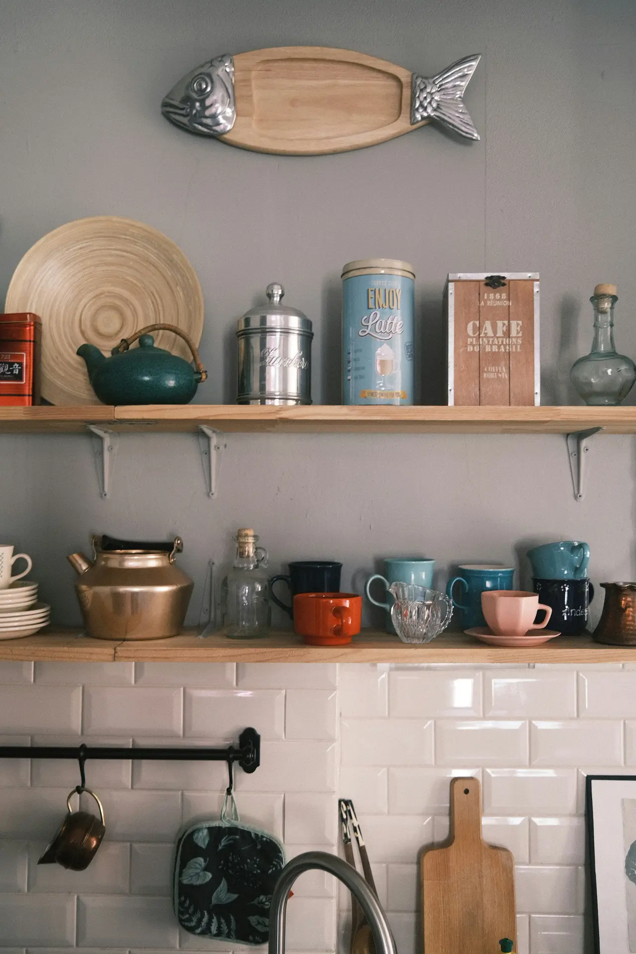 Decorative wall styling in modern farmhouse kitchens highlighting vintage details, with open wooden shelves displaying mixed ceramic mugs, old tins, glass bottles, and metal cookware, set against a white subway tile backsplash for a relaxed, collected look.