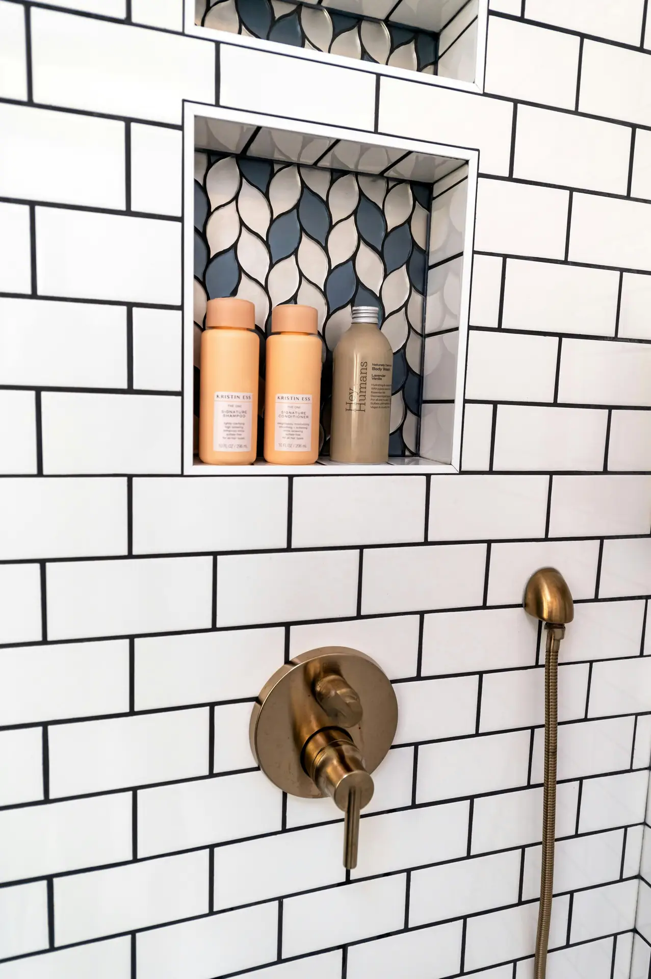 White subway tile shower wall with brass fixtures and a recessed niche in the shower lined with patterned blue and white tiles, neatly holding shampoo and body wash bottles-an elegant example of organization ideas for the bathroom that keeps essentials tidy while adding visual interest.