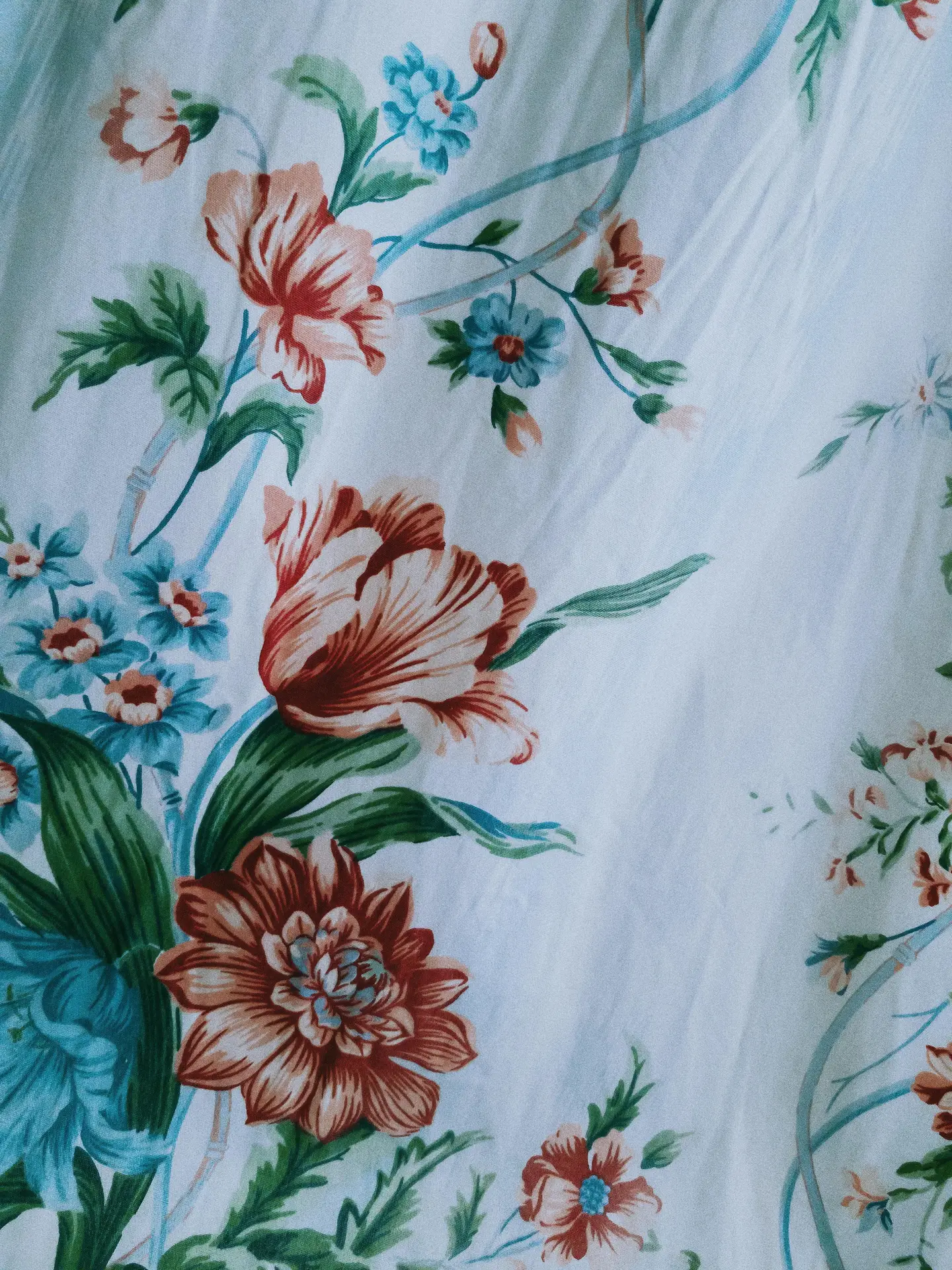 A detailed close-up of a white fabric featuring soft botanical florals in a vintage style. The pattern displays elegant garden flowers, including large terracotta-toned blooms and smaller turquoise blossoms with green leaves, serving as inspiration for classic floral bedding ideas.