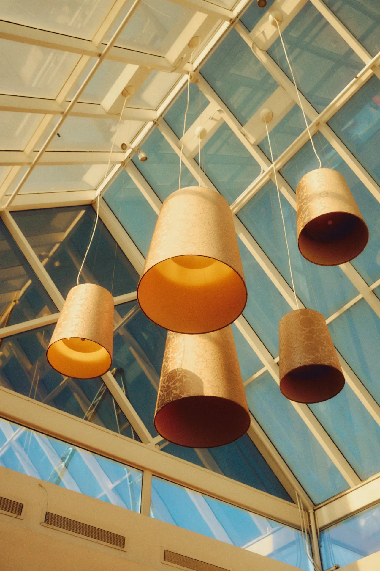 A cozy, cushioned armchair with knitted blankets sits by a large, white-framed window overlooking a lush green garden. A small wooden side table holds an open book and a stylish table lamp, presenting inspiring **sun room ideas**. A textured rattan wall hanging and potted plants complete the tranquil scene. By **implementing lamps for cozy evenings**, this reading nook remains inviting and warm after dusk.