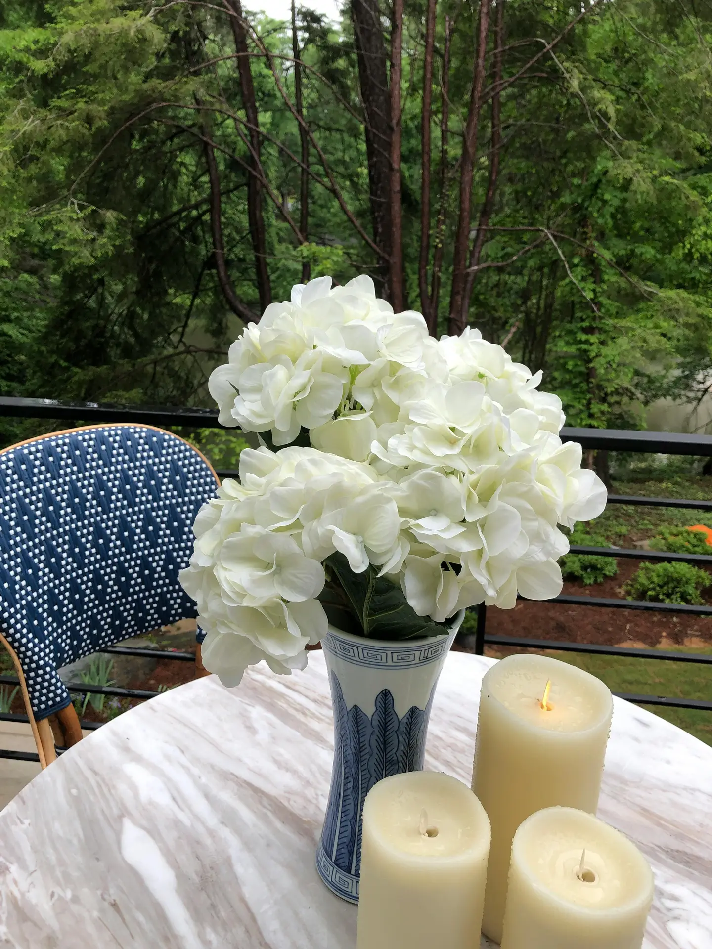 A bright and inviting close-up featuring charming summer decor ideas in a classic white and blue color scheme. On a rustic wooden shelf, a cluster of small ceramic vases holds delicate dried flowers and green foliage. A prominent element is a framed print that displays the words 