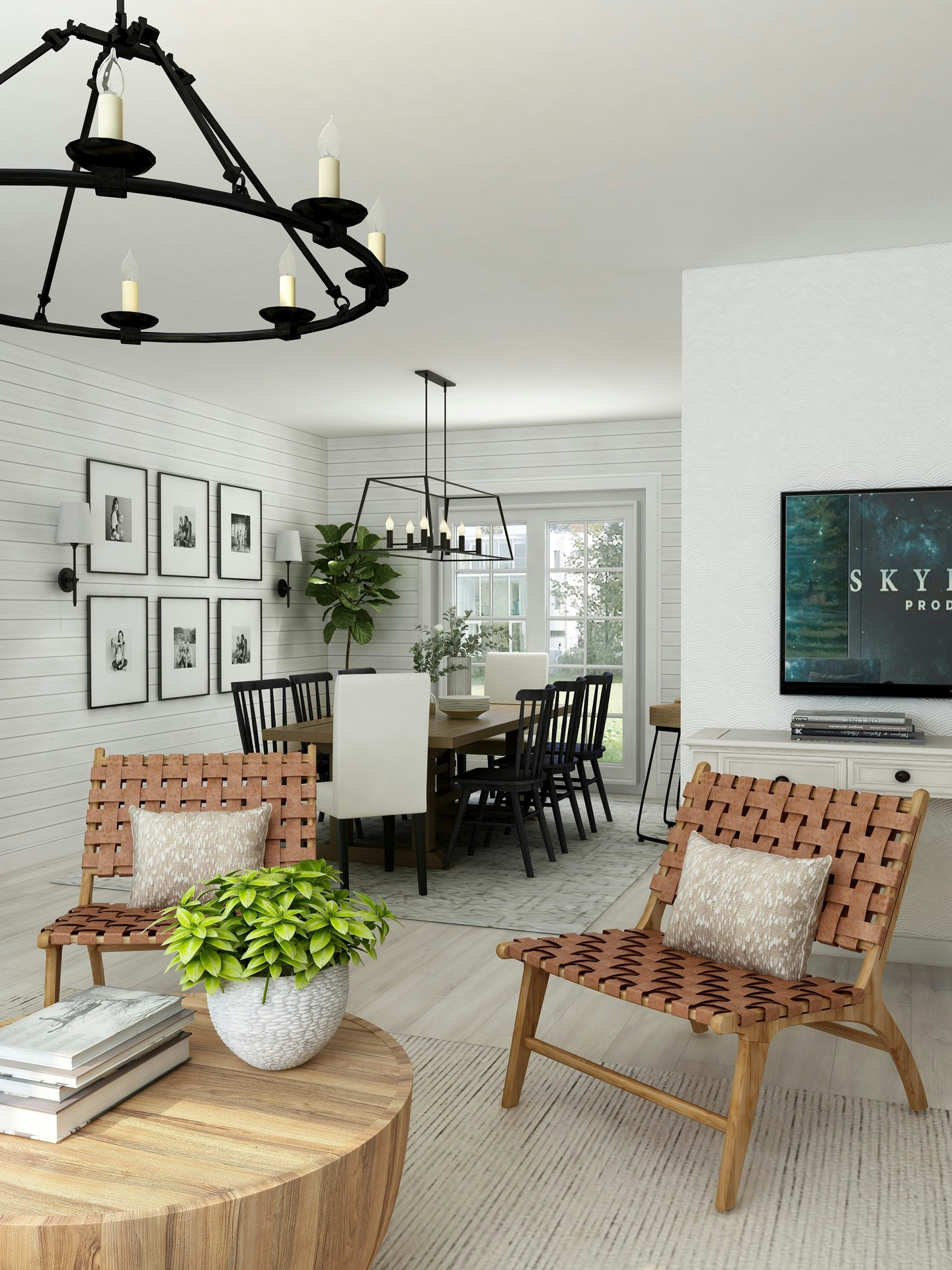 A bright open-concept space beautifully integrates modern summer decor ideas living room styling anchored by sharp black details. In the foreground, two woven tan leather accent chairs with textured pillows sit on a light area rug next to a round wooden coffee table topped with books and a vibrant green potted plant. The adjoining dining space features a long wooden table surrounded by a mix of black and white chairs beneath a geometric black linear chandelier. A large black iron ring chandelier hangs in the upper left, while a grid of six black-framed photos accents the white shiplap walls, giving the breezy summer interior a contemporary, structured finish.