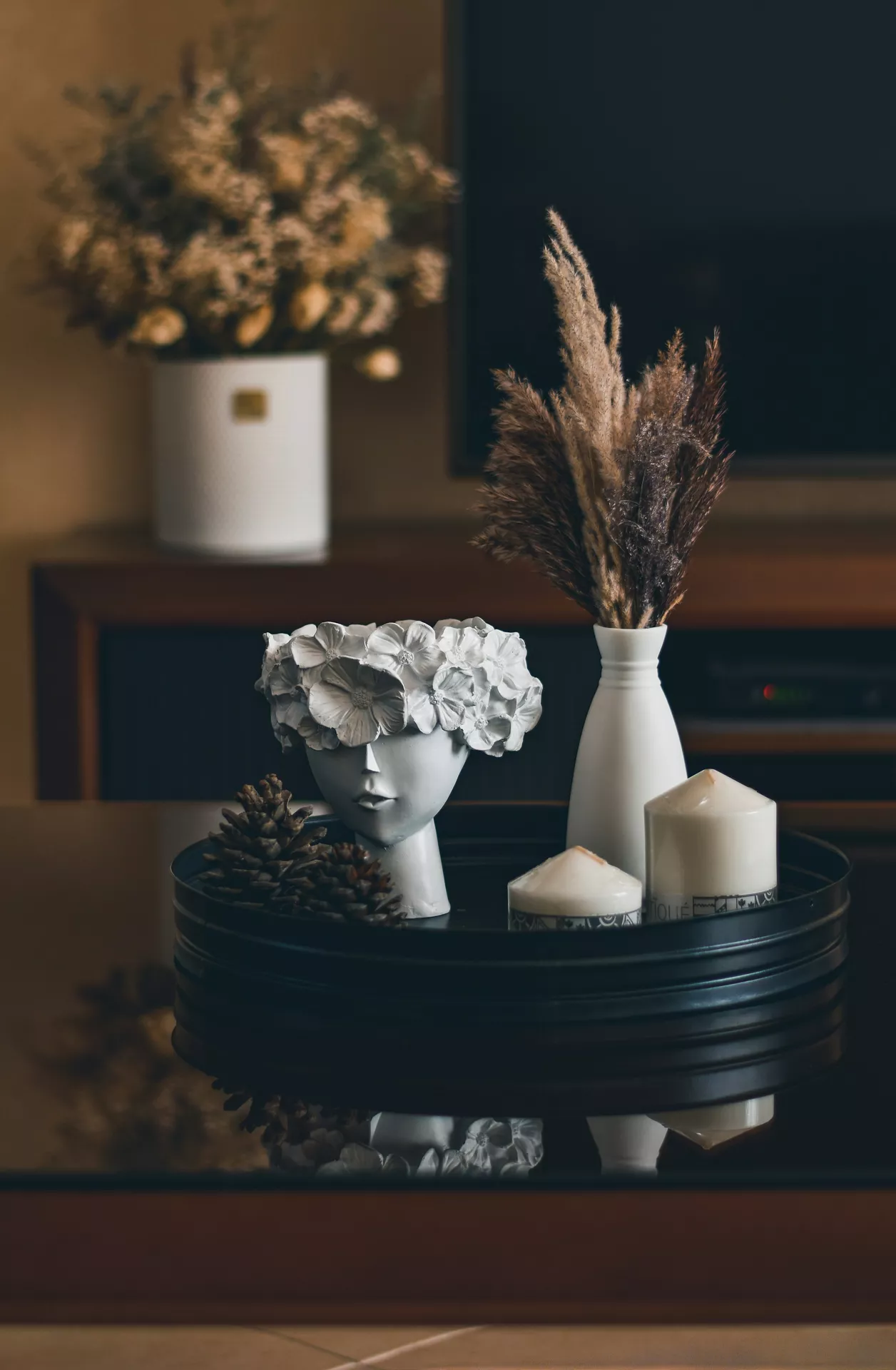 Fall tray decor ideas featuring Floral Head Planter, Vase With Pampas Gras & Candles arranged on a sleek black tray with a decorative floral face planter, soft pampas grass in a white vase, white pillar candles, and pine cones for a cozy modern autumn centerpiece.