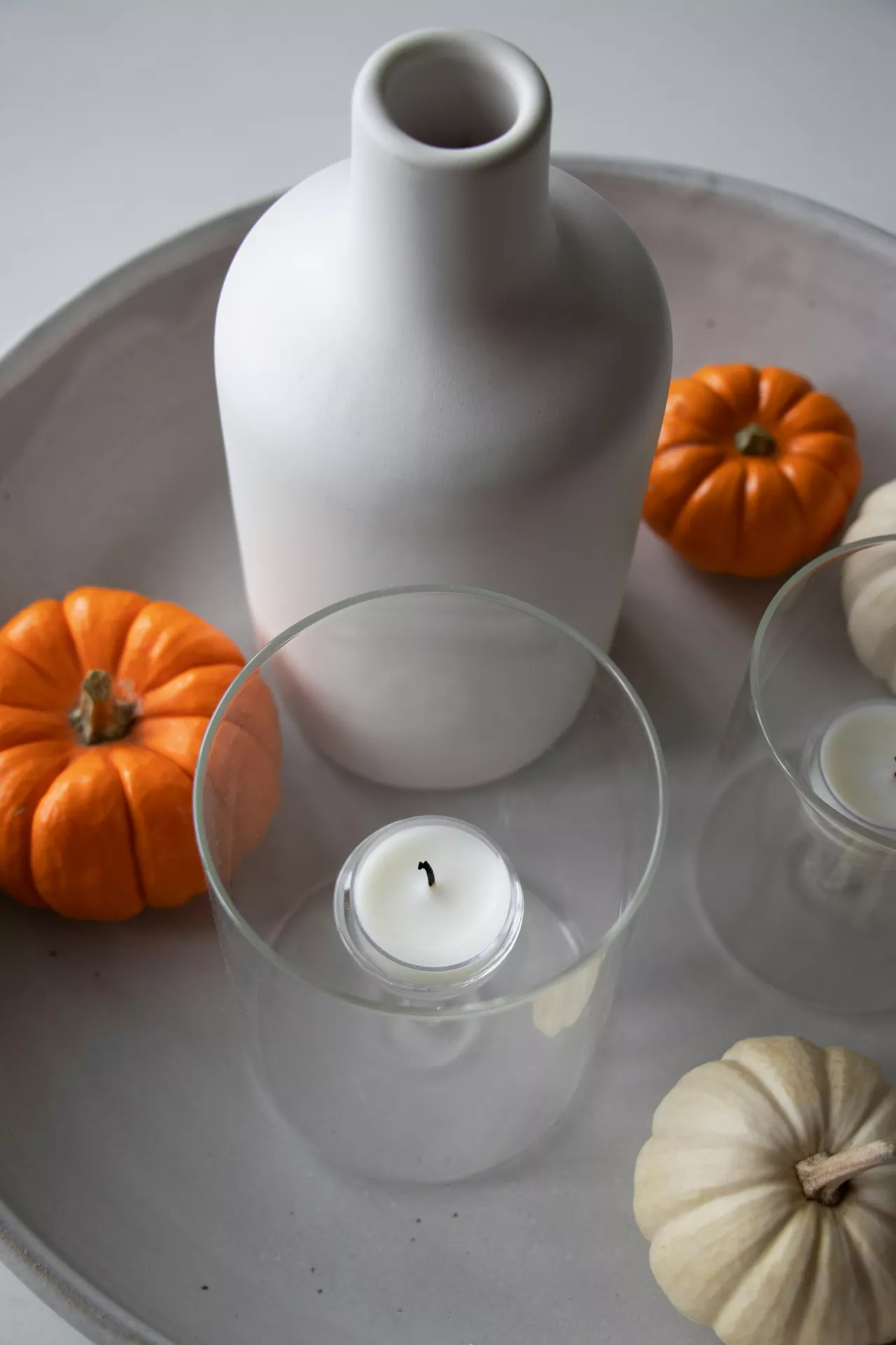 Fall tray decor ideas with Minimalist Decor featuring a matte white vase, clear glass candle holders, and a mix of orange and white mini pumpkins arranged on a neutral tray for a clean, elegant autumn centerpiece.