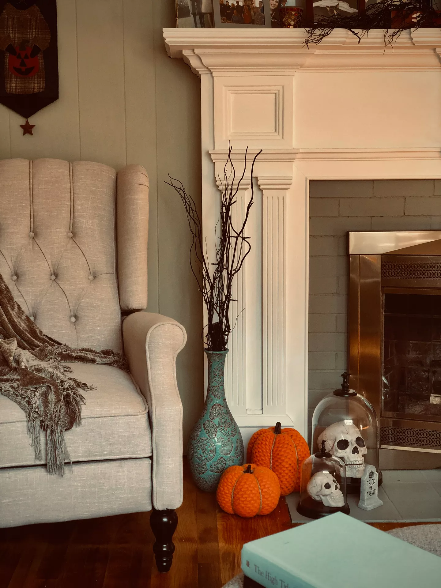 Cozy living room with elegant Halloween mantel decor featuring decorative skulls under glass cloches, knitted pumpkins, black branches in a tall vase, and subtle spooky accents around a white fireplace. This inviting seasonal setup offers timeless Halloween Decor Ideas that blend festive charm with sophisticated fall styling.