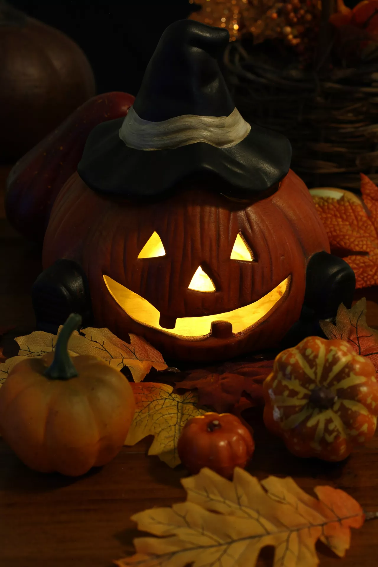 Glowing Halloween pumpkin wearing a black witch hat, surrounded by colorful gourds, autumn leaves, and warm candlelight for a cozy seasonal display. This charming arrangement is full of Halloween Decor Ideas, with a classic halloween pumpkin and leaves theme that creates a festive fall centerpiece.