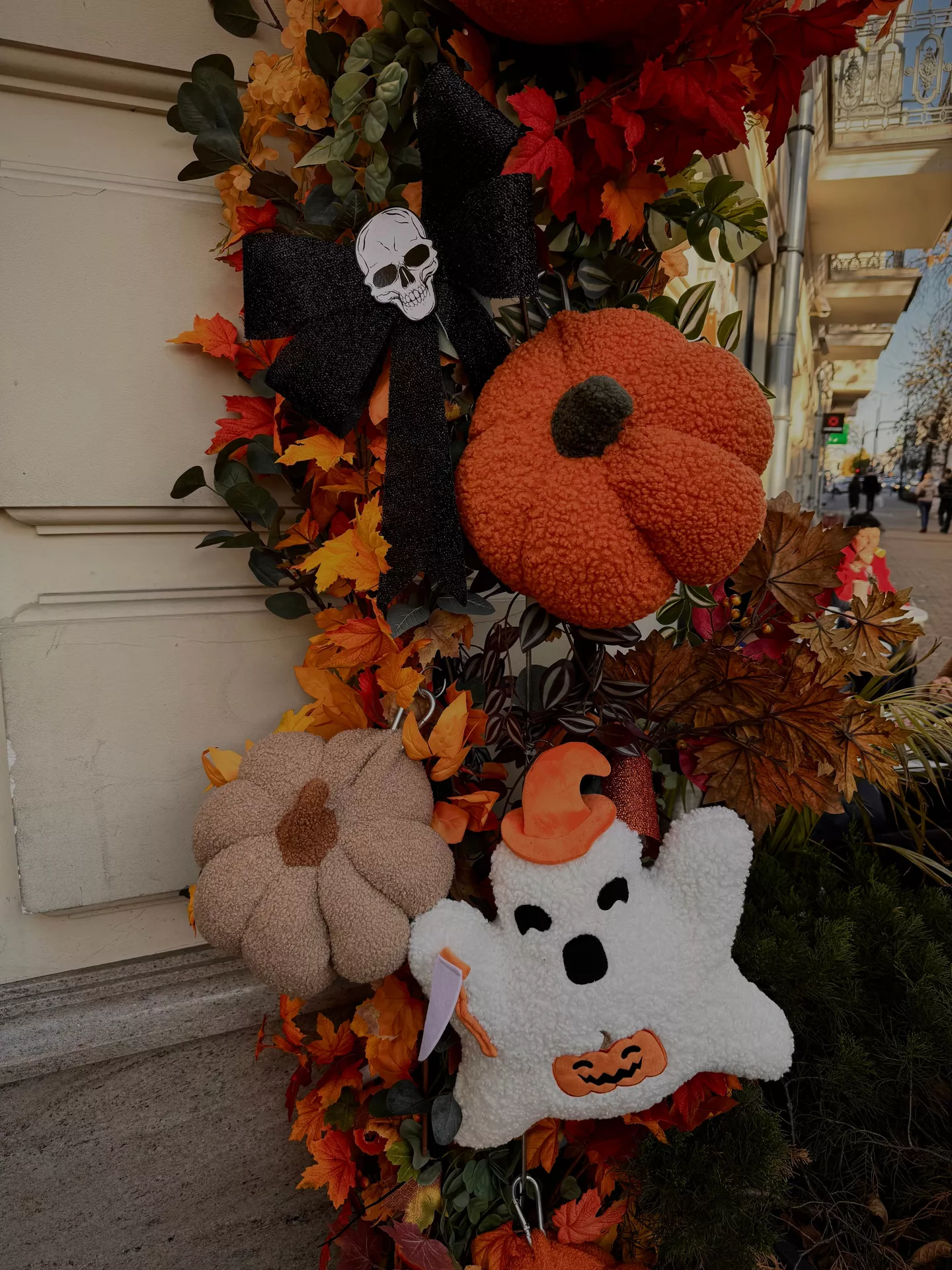 Colorful fall entry display with a plushy garland featuring soft pumpkins, a smiling ghost, autumn leaves, and a black skull bow wrapped around a porch column. This festive arrangement combines cozy textures and playful accents for charming Halloween Decor Ideas with a whimsical plushy garland.