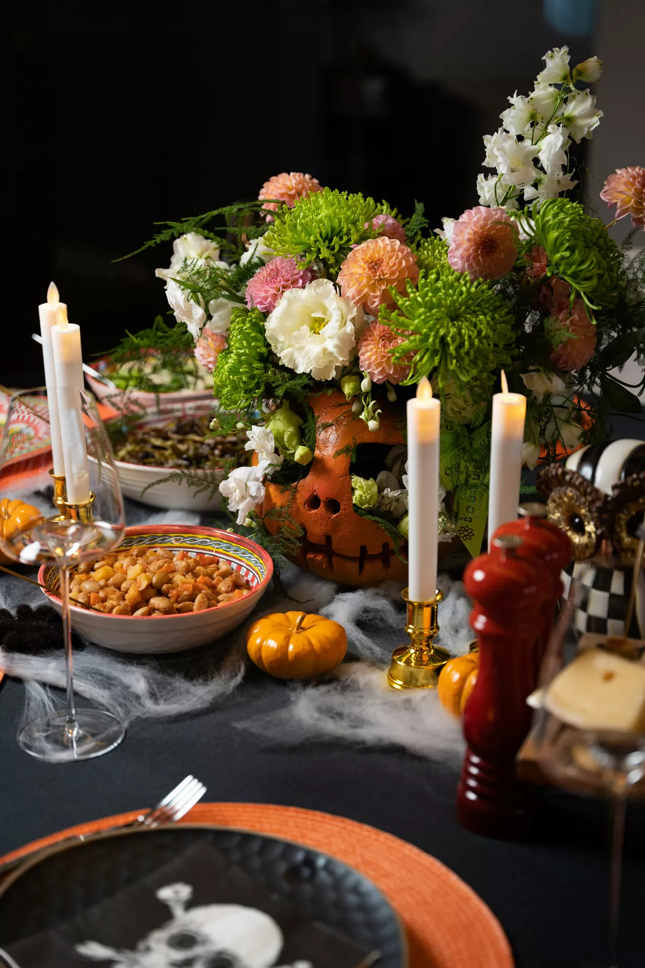 Festive Halloween dining table featuring a carved pumpkin as flower vase filled with fresh blooms, surrounded by candles, mini pumpkins, cobweb accents, and seasonal tableware. This elegant centerpiece combines cozy fall colors with creative Halloween Decor Ideas, showcasing a unique pumpkin as flower vase for a memorable holiday tablescape.