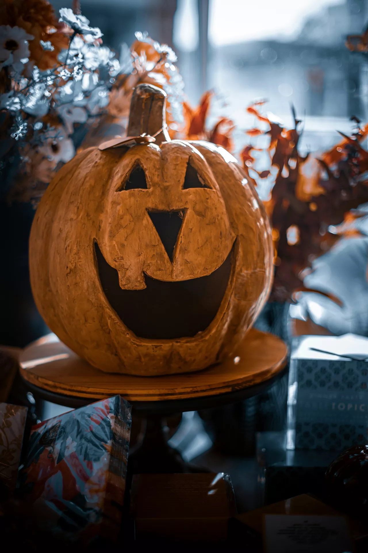 Rustic pumpkin carved from wood with a classic jack-o'-lantern face displayed on a wooden pedestal, surrounded by autumn flowers and seasonal decor indoors. This charming centerpiece adds handcrafted character to Halloween Decor Ideas and showcases a unique pumpkin carved from wood for cozy fall decorating.