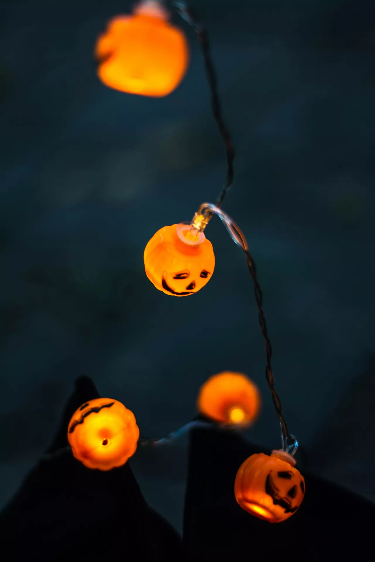 Halloween Decor Ideas with glowing pumpkin lanterns strung on a light garland, featuring tiny jack-o'-lantern faces that create a warm and festive Halloween atmosphere against a dark evening background.