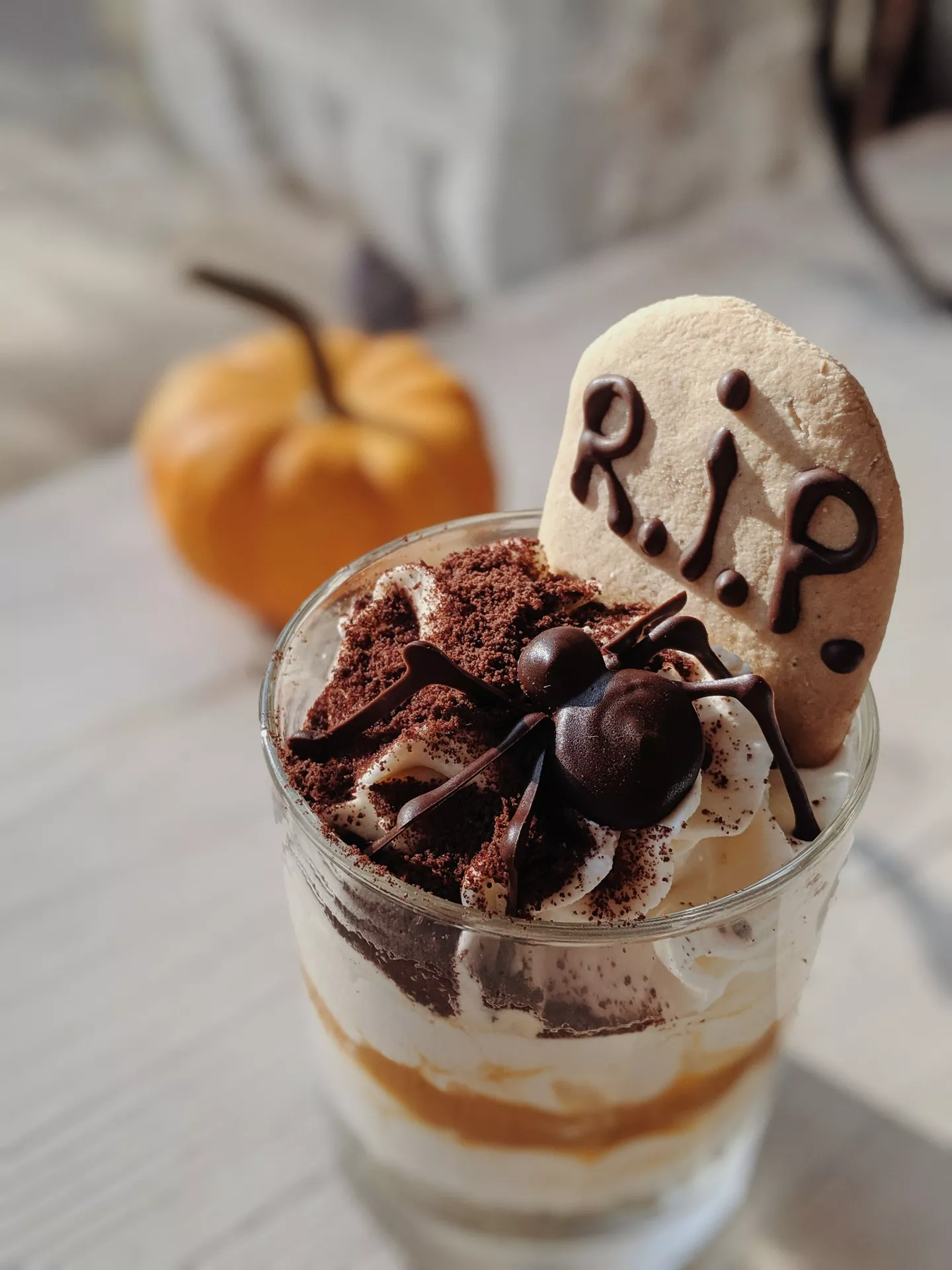 Halloween Party Food Ideas featuring a spooky graveyard dirt dessert cup layered with creamy filling, cookie crumbs, whipped cream, a chocolate spider, and a RIP cookie for a fun and festive Halloween treat.
