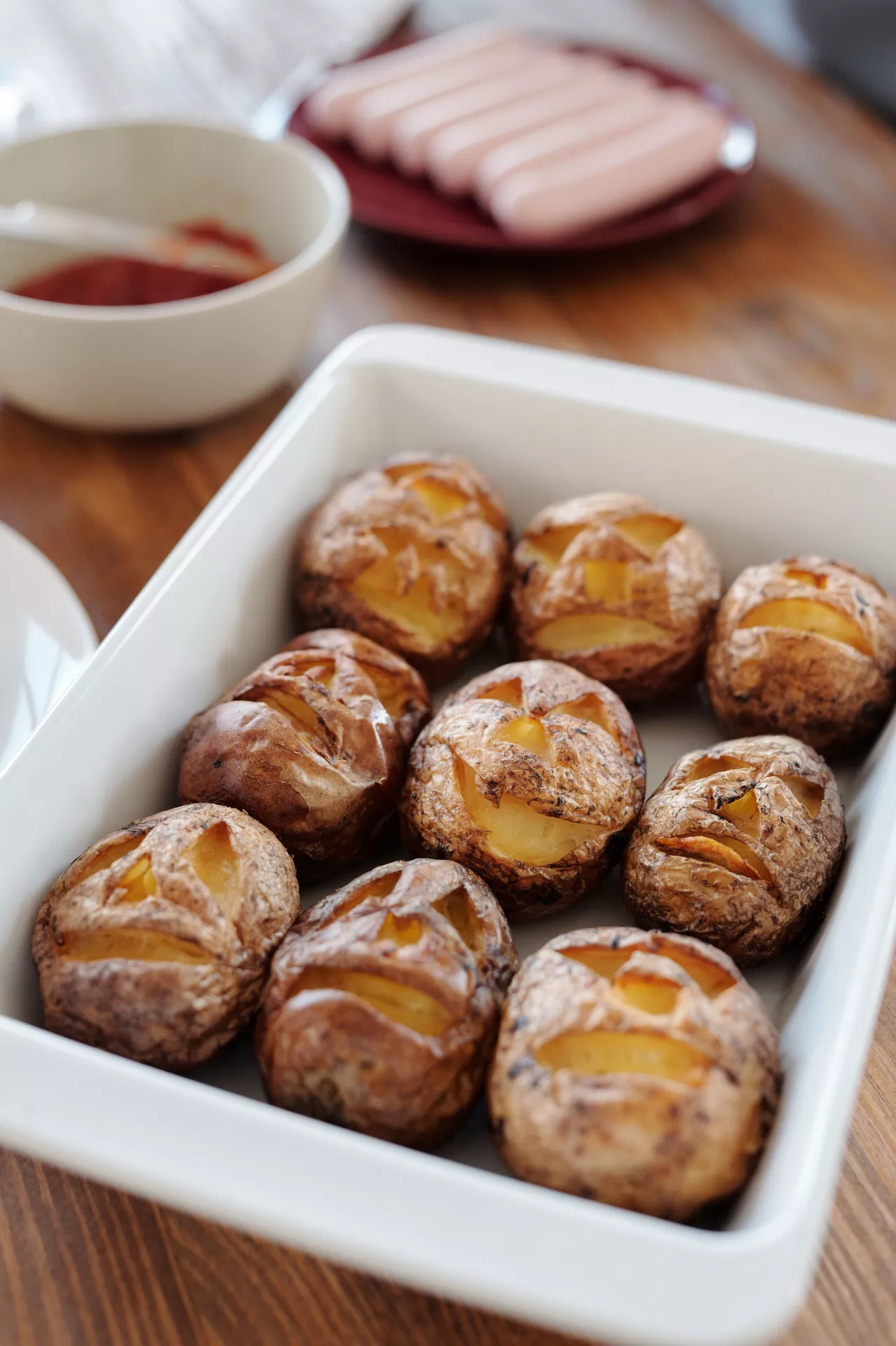 Halloween Party Food Ideas featuring jack o'lantern baked potatoes carved with spooky faces, served in a baking dish with ketchup and hot dogs in the background for a fun and kid-friendly Halloween meal.
