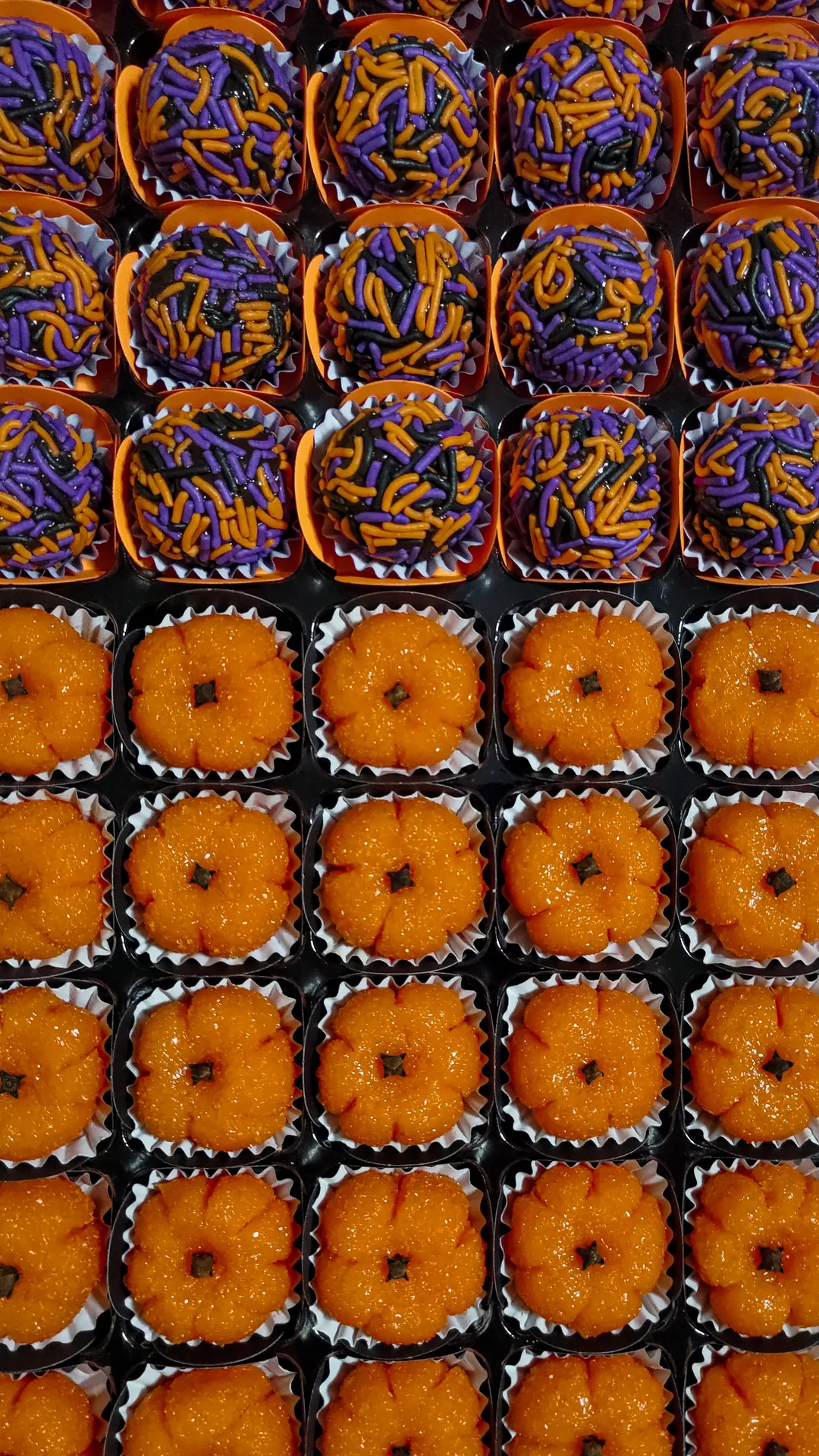 Halloween Party Food Ideas featuring colorful purple and pumpkin shaped muffins decorated with orange, purple, and black sprinkles, neatly arranged in rows for a festive Halloween dessert table.