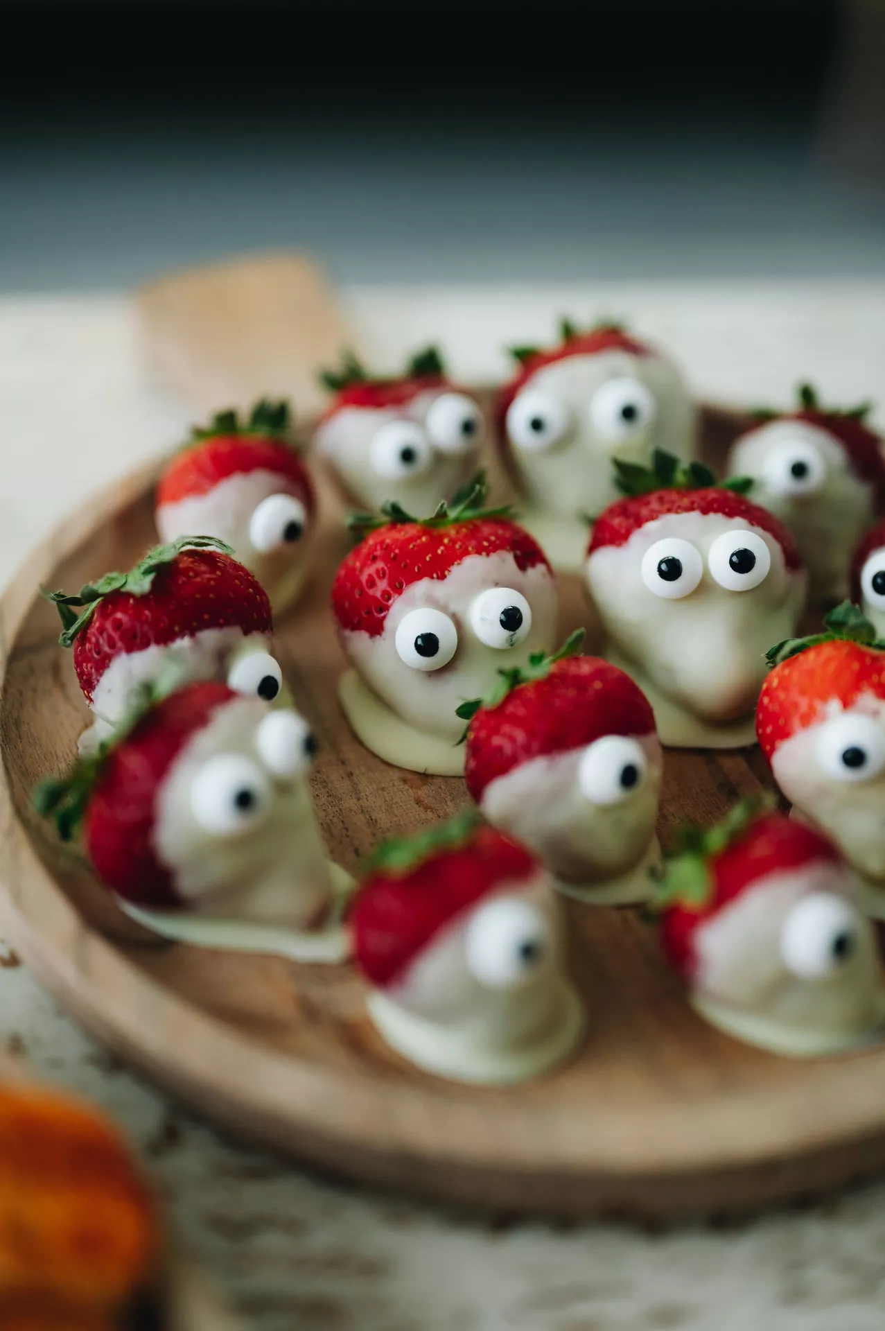 Halloween Party Food Ideas featuring spooky strawberries dipped in white chocolate and decorated with candy eyes, arranged on a wooden serving board for a fun and kid-friendly Halloween dessert.