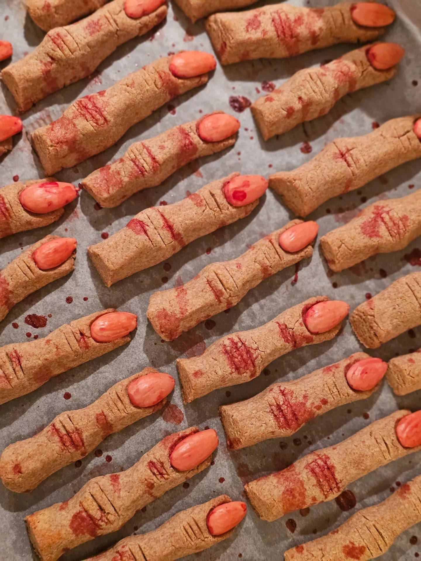 Halloween Party Food Ideas featuring spooky witch finger cookies decorated with almond fingernails and realistic red icing details, arranged on a baking tray for a creepy and festive Halloween dessert spread.