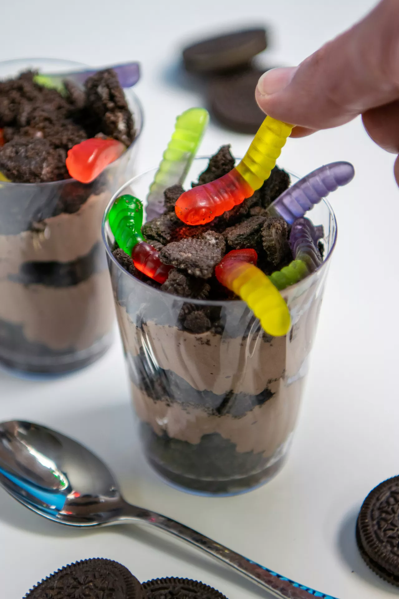 Halloween Party Food Ideas featuring a chocolate worm dessert layered with crushed chocolate cookies and pudding, topped with colorful gummy worms for a fun and spooky Halloween treat.