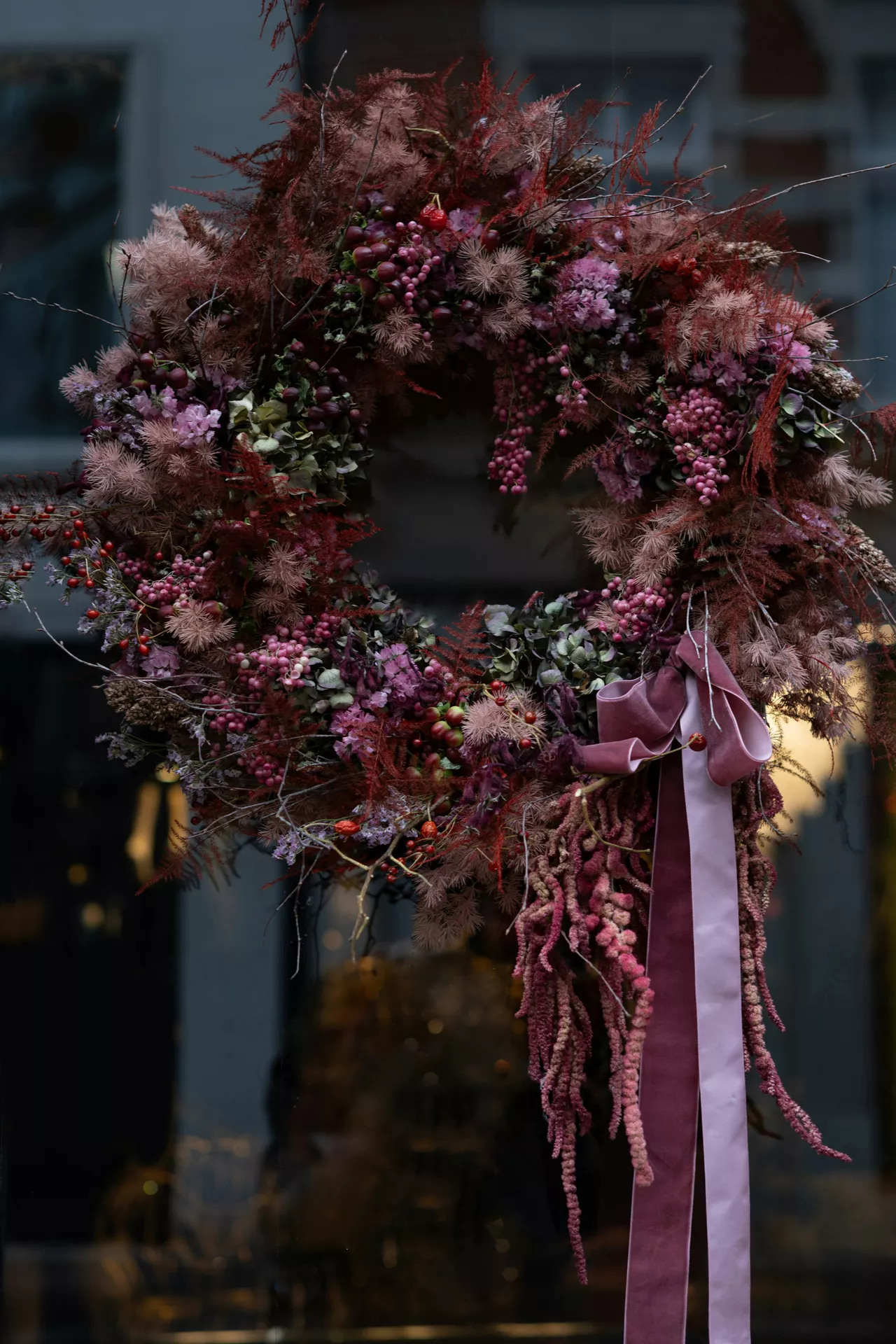 Fall decor wreaths featuring a Burgundy Wreath Featuring Amaranthus, Hydrangeas & Berries with lush dried florals, rich burgundy foliage, pink berries, hydrangeas and flowing velvet ribbons hanging on a front door for an elegant autumn entrance.