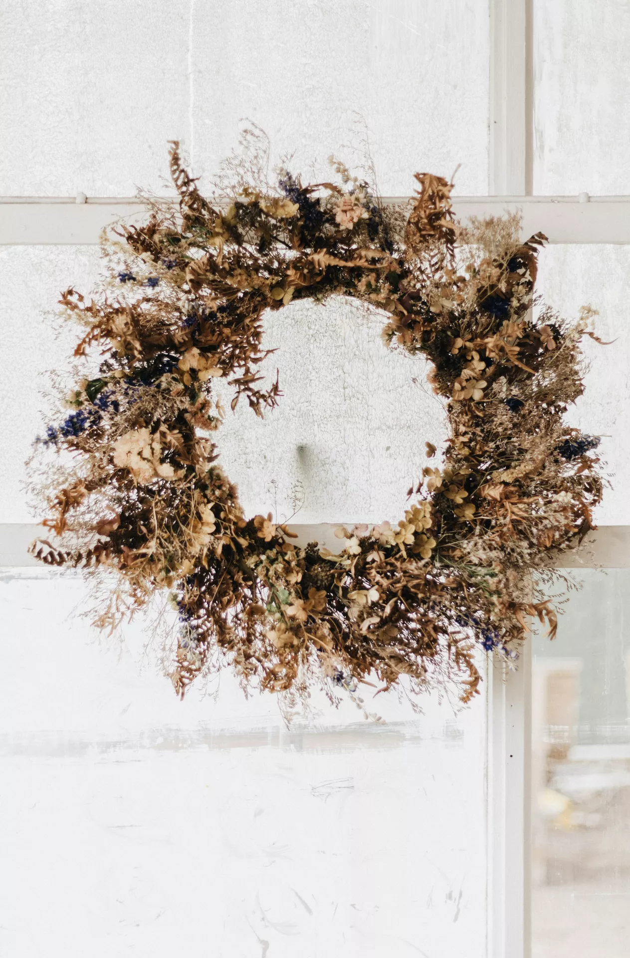 Fall decor wreaths featuring a dried flower wreath made with preserved grasses, delicate florals and natural foliage, hanging on a white glass door to create a soft, rustic and timeless autumn entrance.