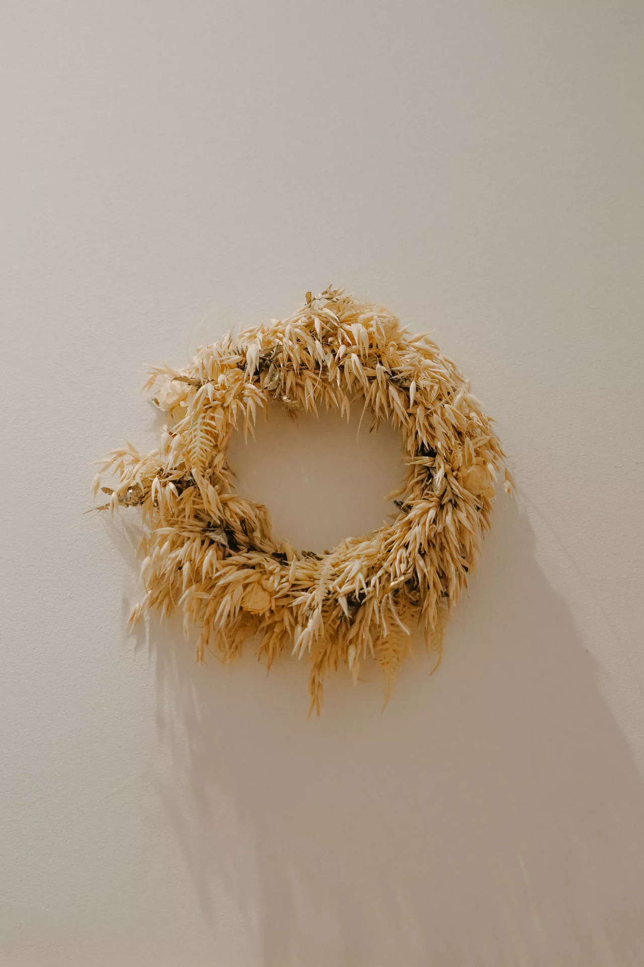 Fall decor wreaths featuring a Minimalist Scandinavian Dried Oat Wreath made from natural dried oat stems, creating a simple and elegant neutral autumn display on a white wall with warm organic texture.