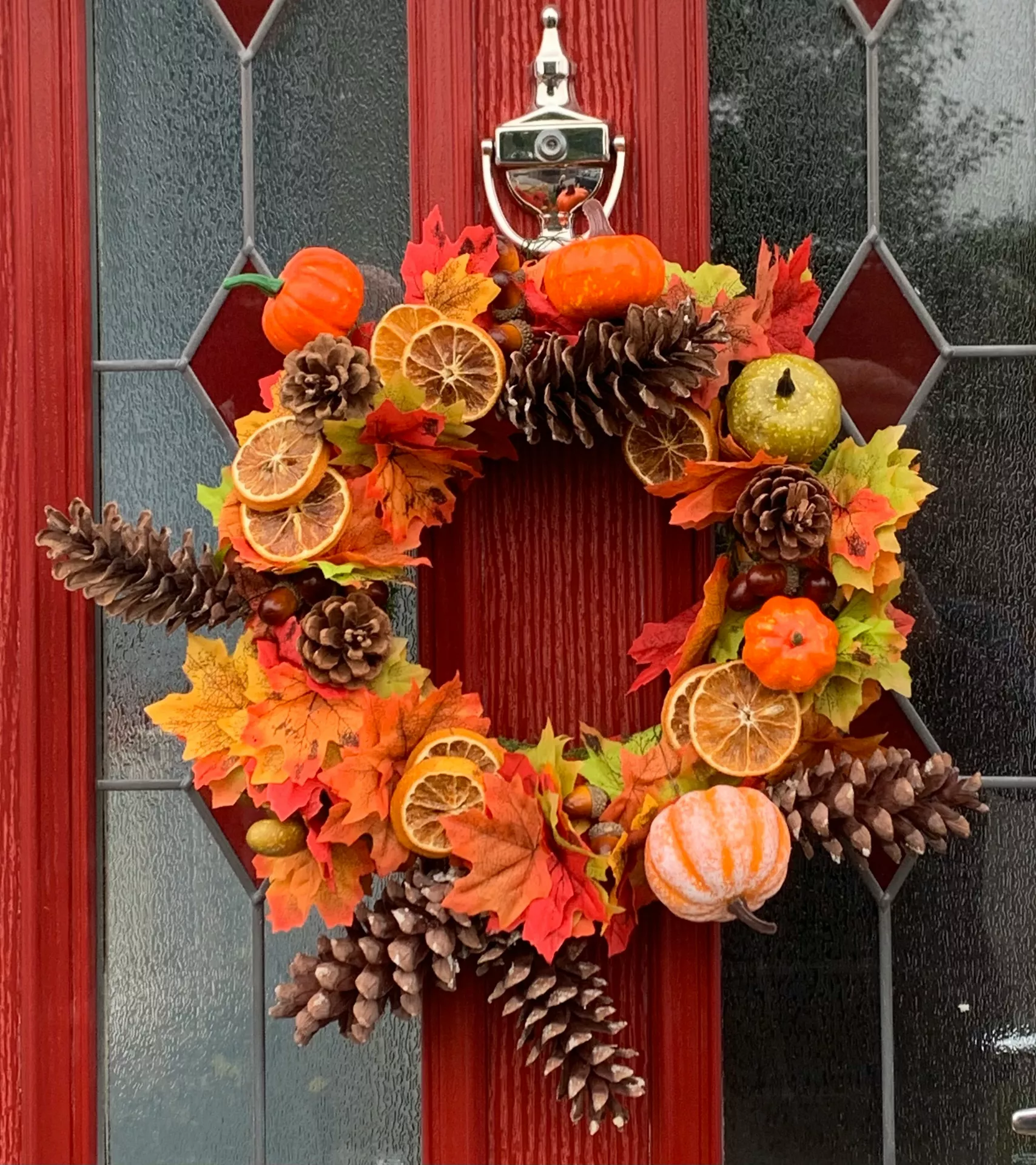 Fall decor wreaths featuring Orange Leaves, Pine Cones, Dried Orange Slices & Pumpkins, beautifully arranged on a red front door with colorful autumn foliage, miniature pumpkins, pine cones, and citrus slices for a warm seasonal entrance.