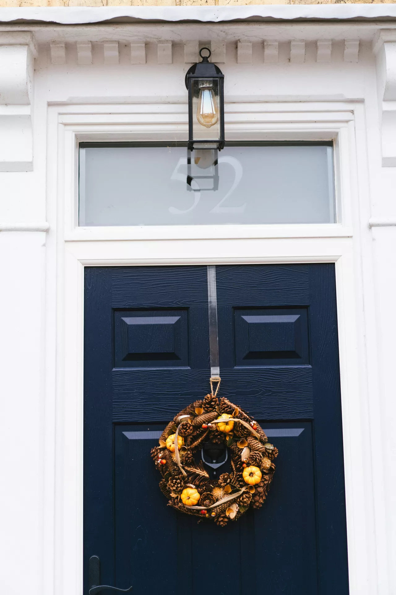 Fall decor wreaths featuring pine cones, spruce cones and pumpkins, beautifully arranged on a natural wreath hanging from a navy blue front door, creating a warm and welcoming autumn entrance with rustic seasonal accents.