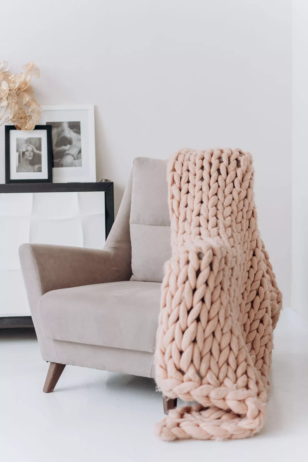 Fall living room decor ideas featuring a cozy blanket in chunky knit fabric draped over a neutral armchair, creating a soft and inviting autumn atmosphere.