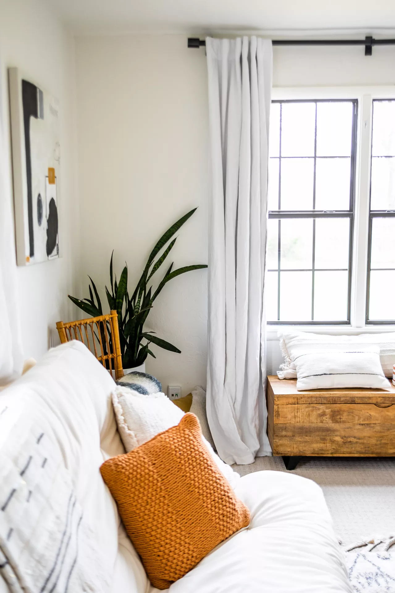 Fall living room decor ideas featuring a bright white sofa styled with cushions in fall color, including a warm burnt orange knitted pillow, neutral textiles, a wooden window bench, and green plants.